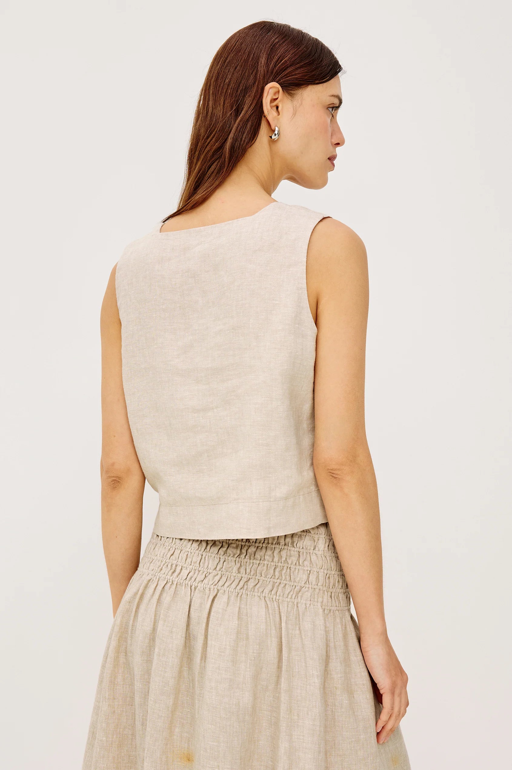 Woman wearing a beige sleeveless top and skirt set on a plain background