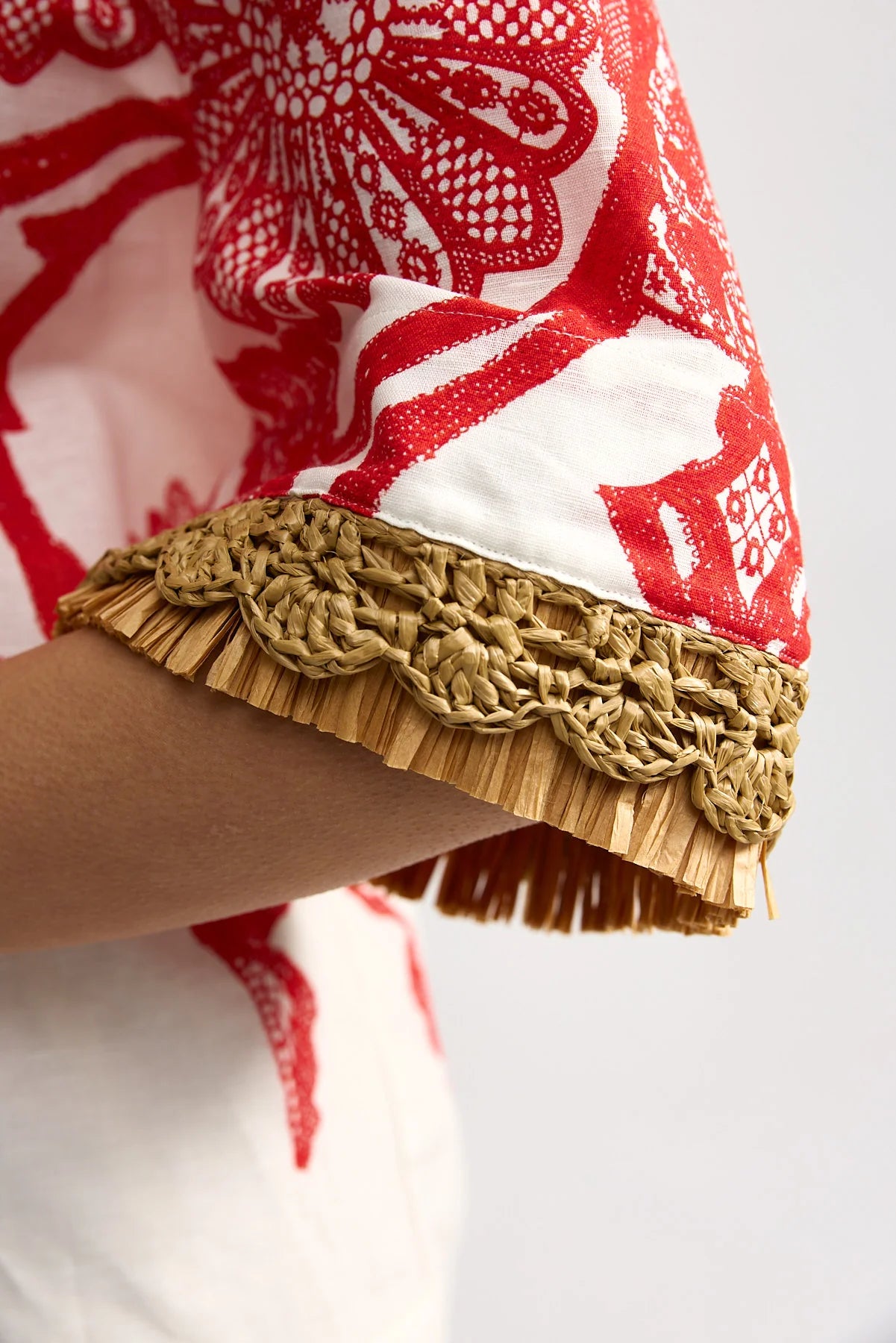 Close-up of a red and white patterned garment with a gold fringe trim on a white background
