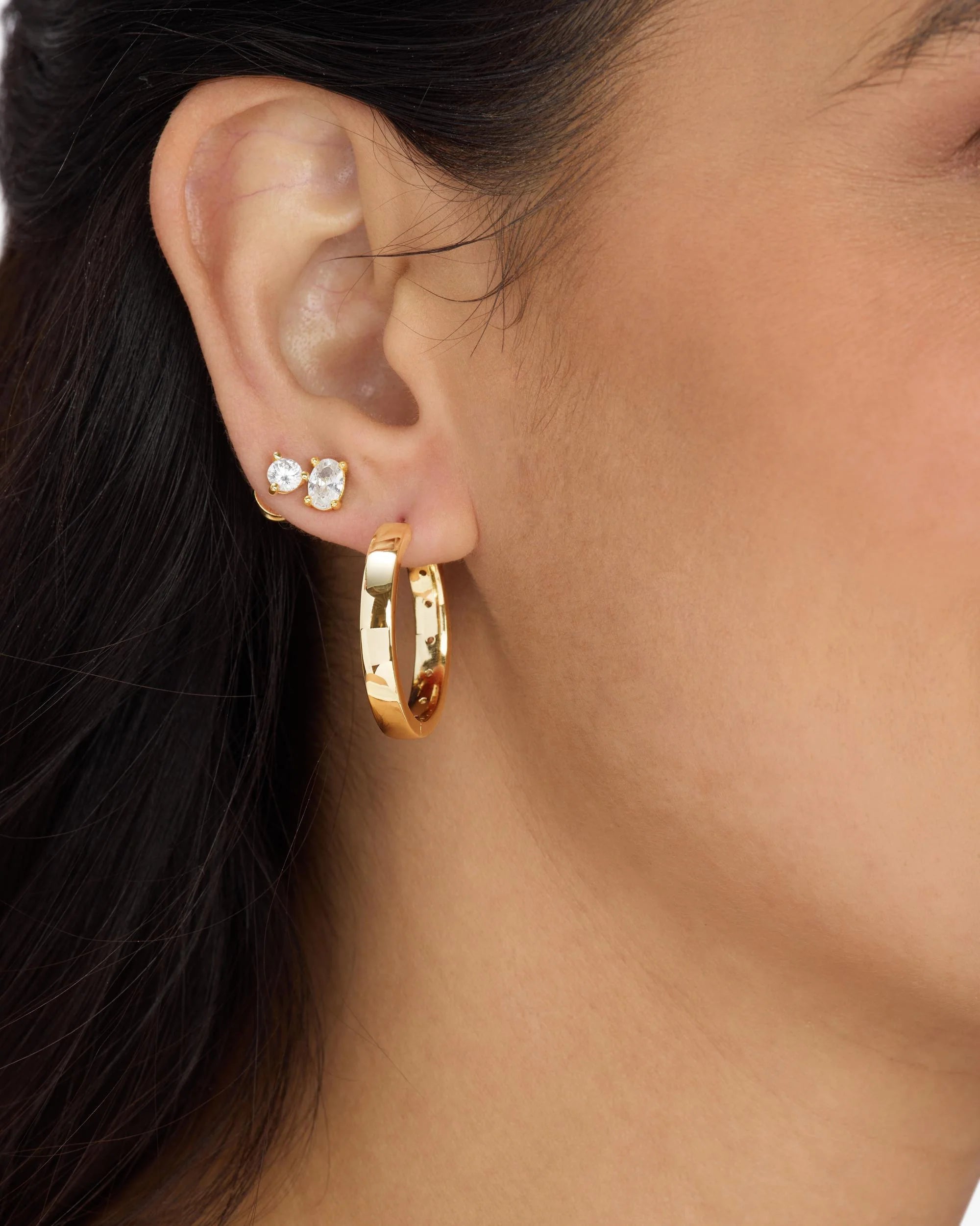 Close-up of an ear wearing gold hoop earrings with a blurred background