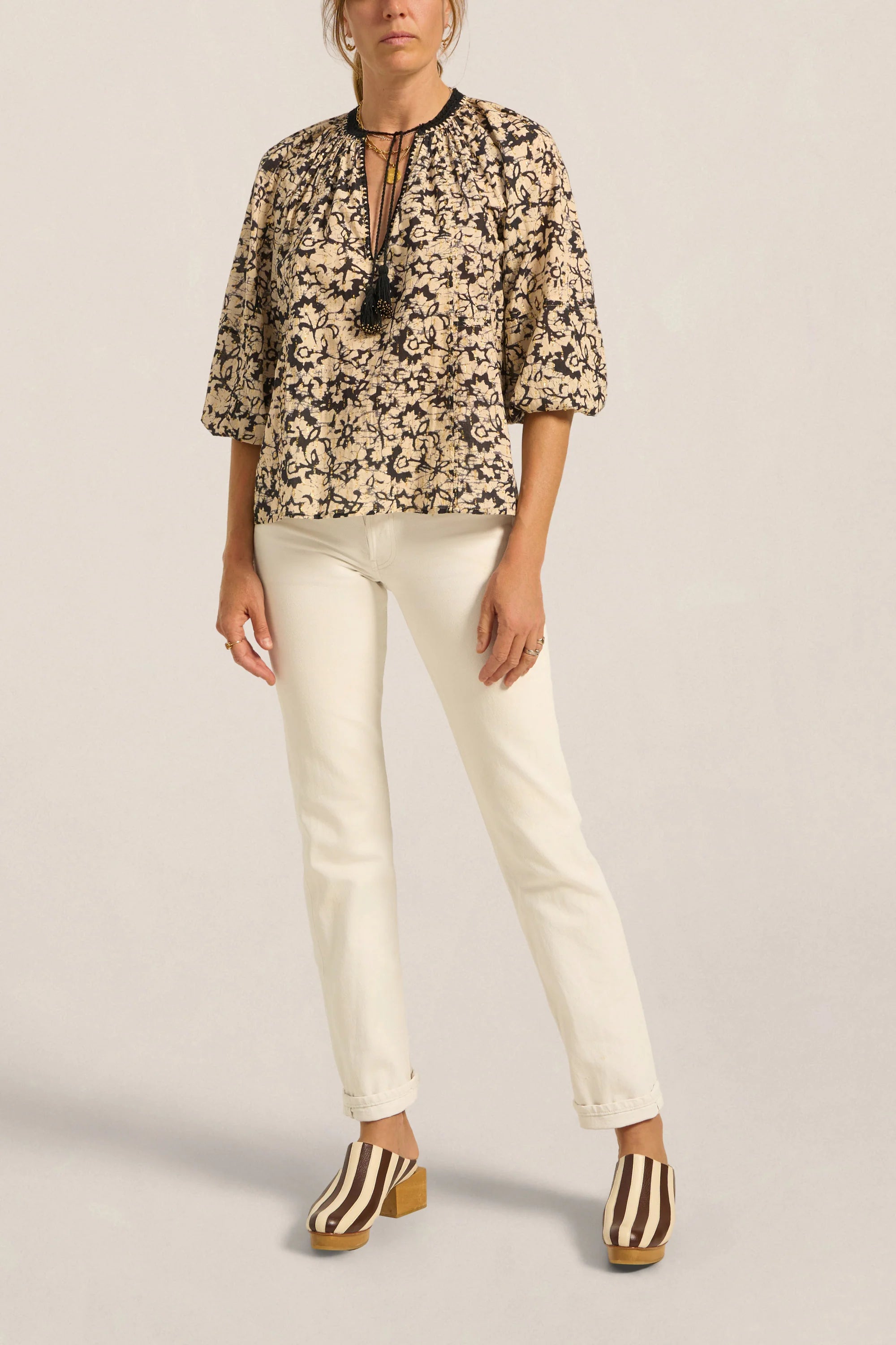 Woman wearing a floral blouse and white pants on a plain background