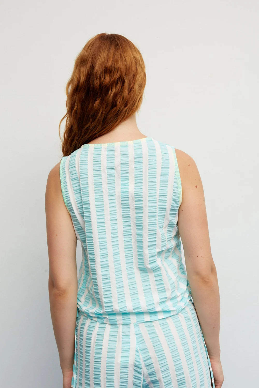 Woman wearing a sleeveless dress with vertical stripes against a plain background