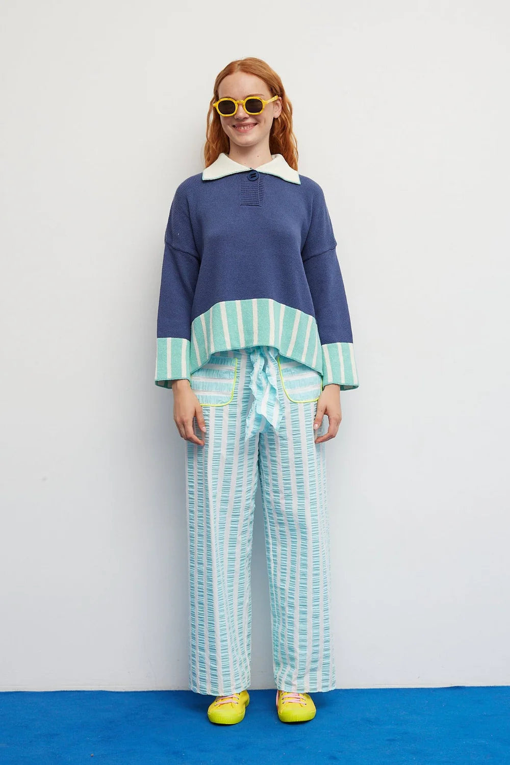 Person wearing a blue and white top with green and white striped pants on a white background