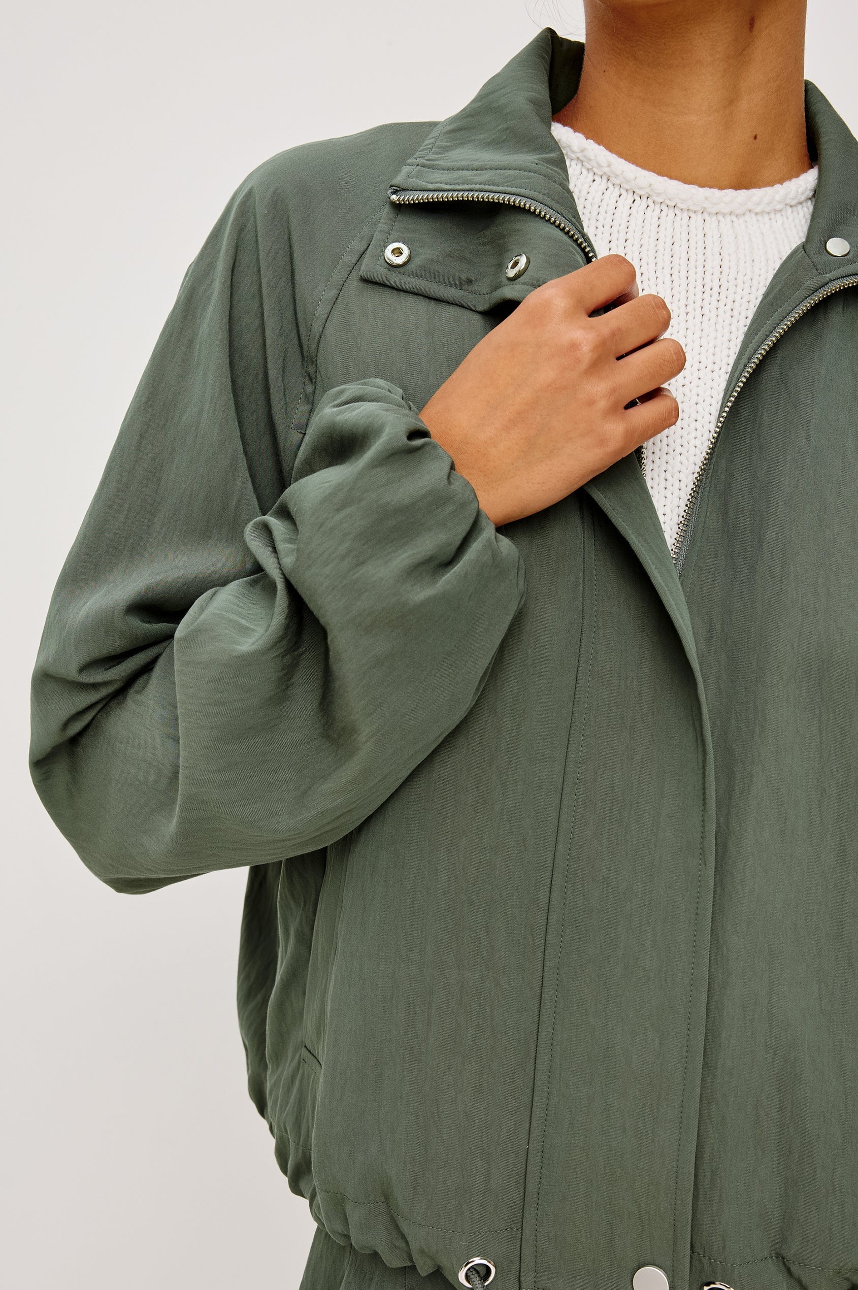 Person wearing a green jacket with a white shirt underneath on a light gray background