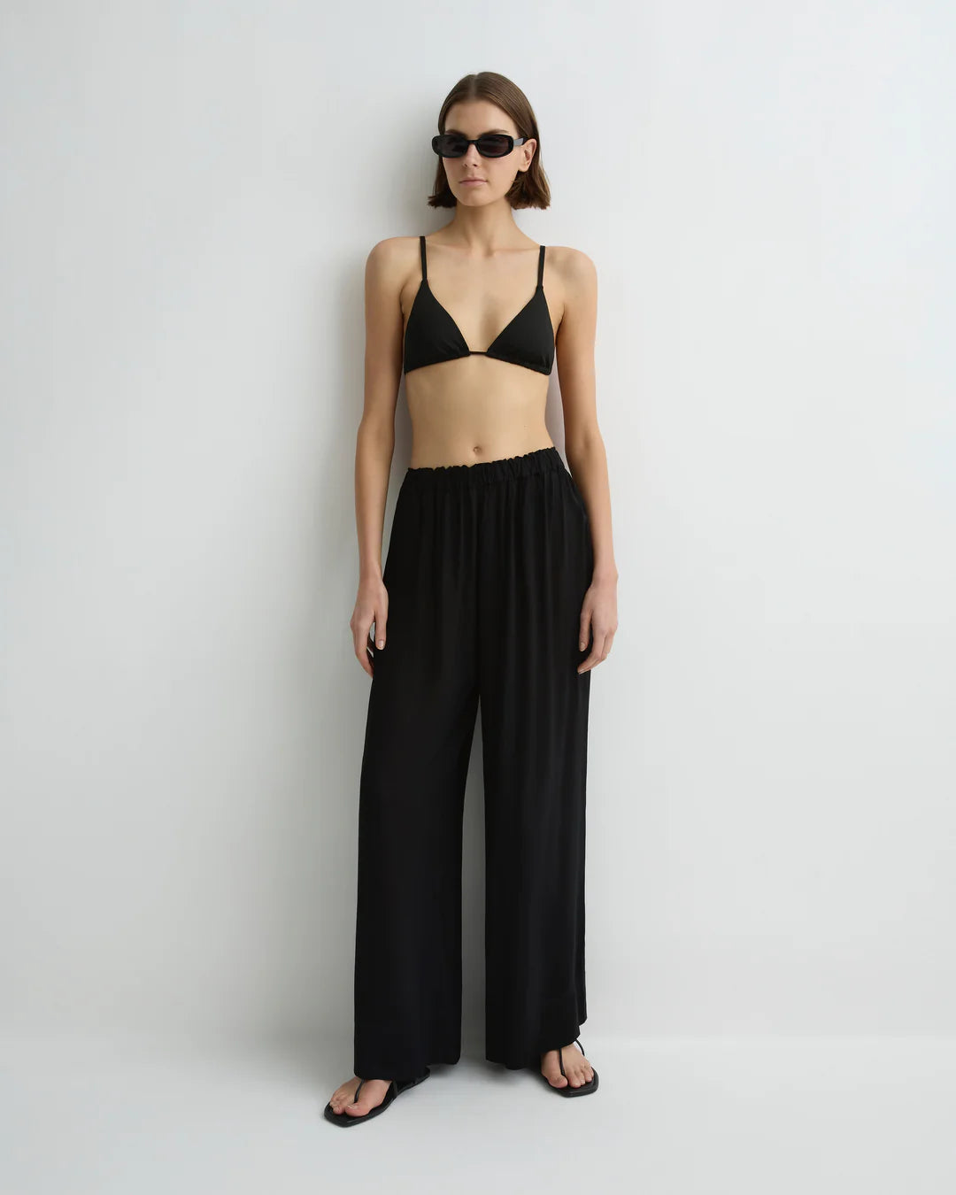 Woman wearing a black bikini and wide-leg pants on a white background