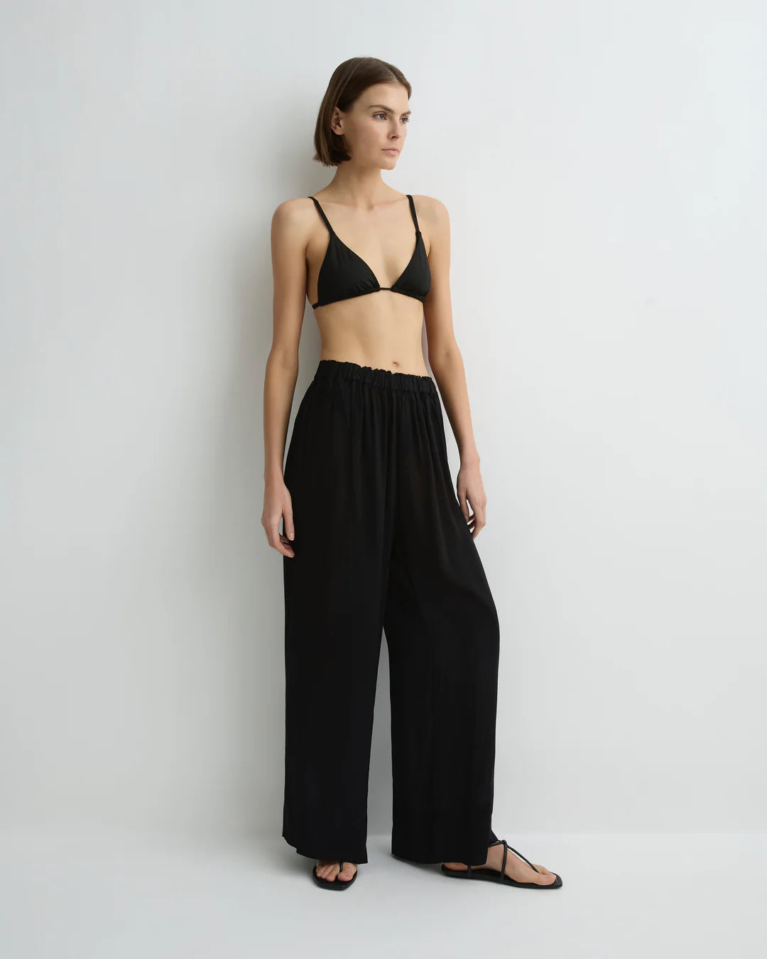 Woman wearing a black outfit with wide-leg pants and a bralette against a white background