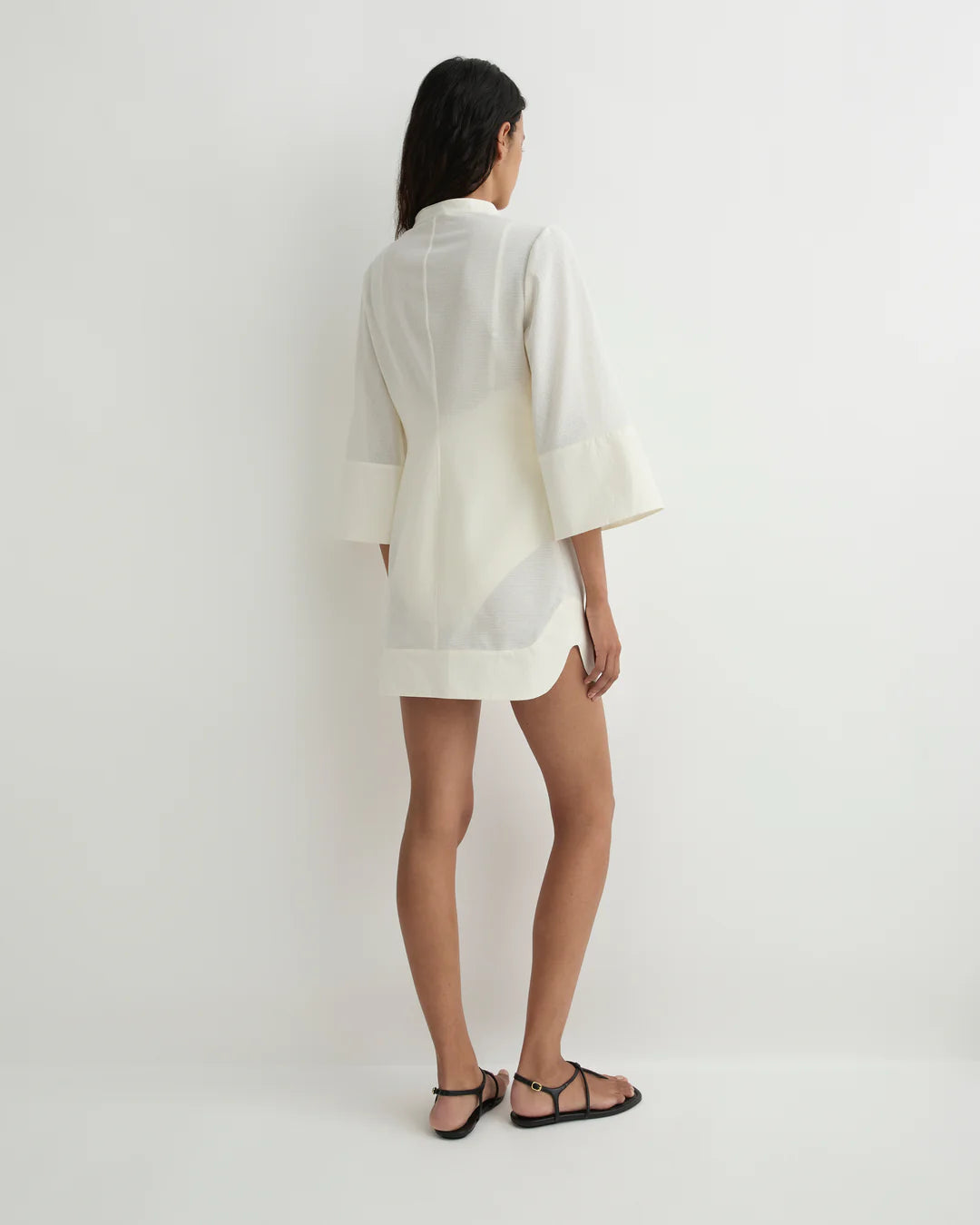 Person wearing a white shirt and black sandals on a plain background