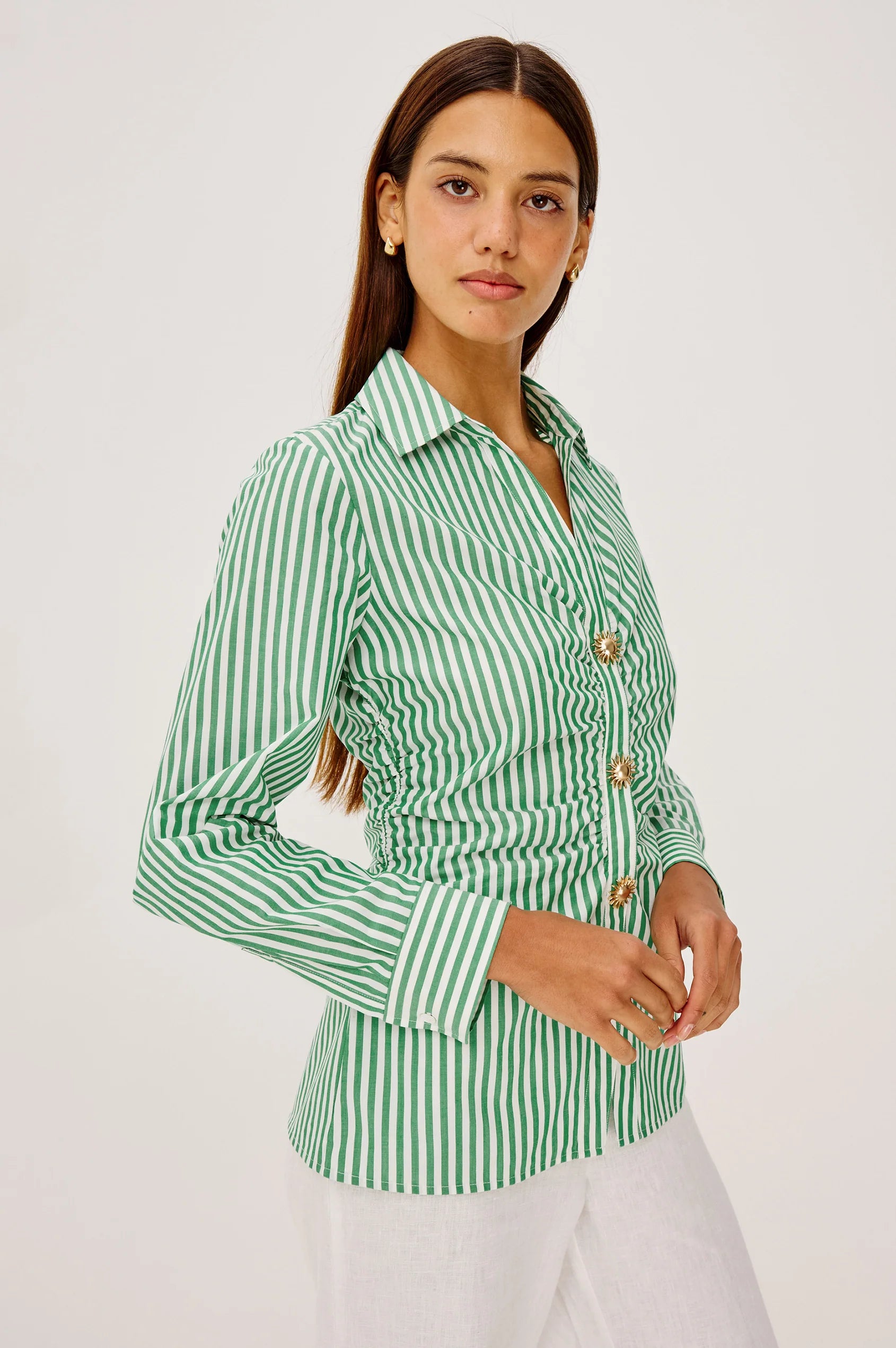 Woman wearing a green and white striped shirt with gold buttons on a white background