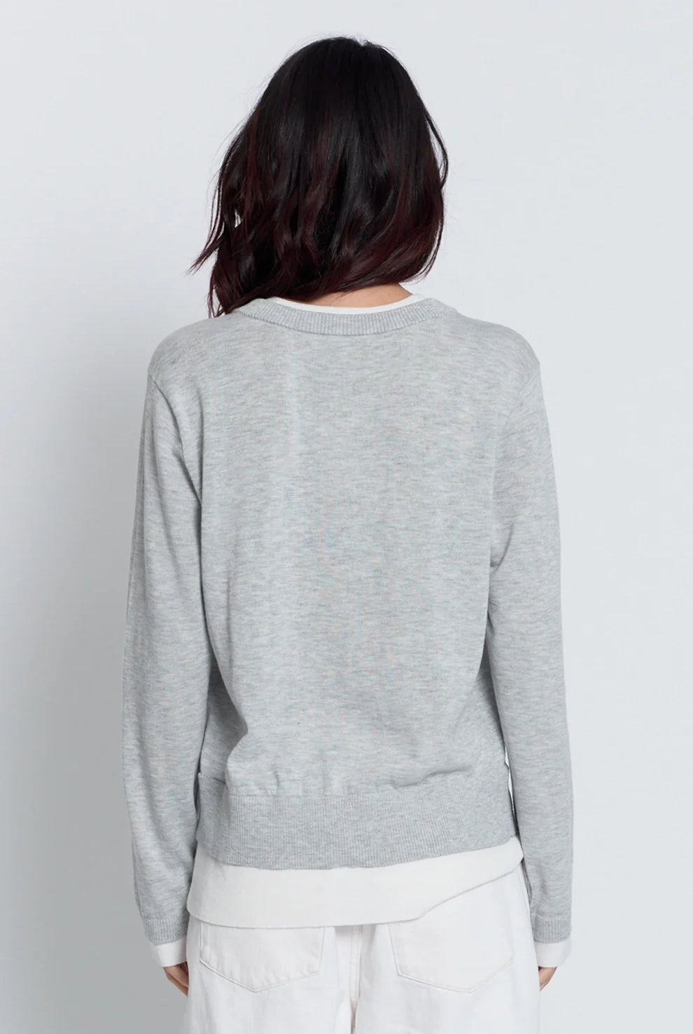 A person shown from the back wearing a light heather gray long-sleeve top with a white undershirt and white pants, against a plain light gray studio background.