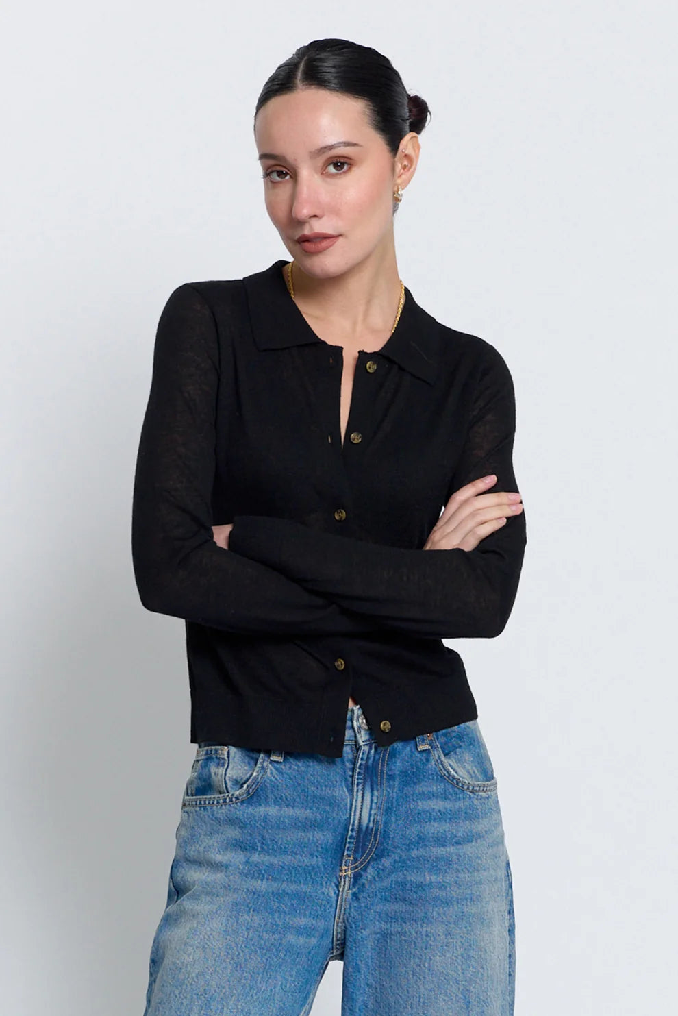 A woman modeling a black long-sleeve knit polo cardigan with brown buttons, paired with blue jeans, against a light gray studio background.