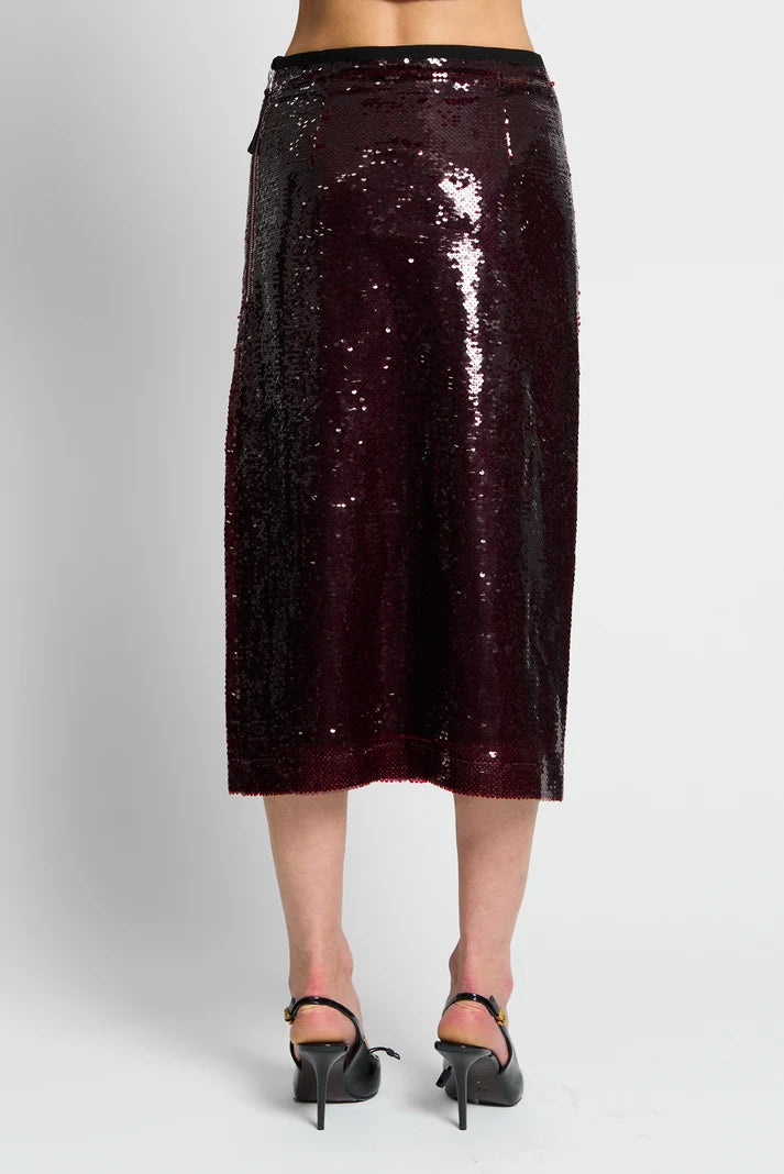 A dark burgundy sequined midi skirt worn by a model, shown from the waist down against a light gray studio background. The model is also wearing black high-heeled sandals.