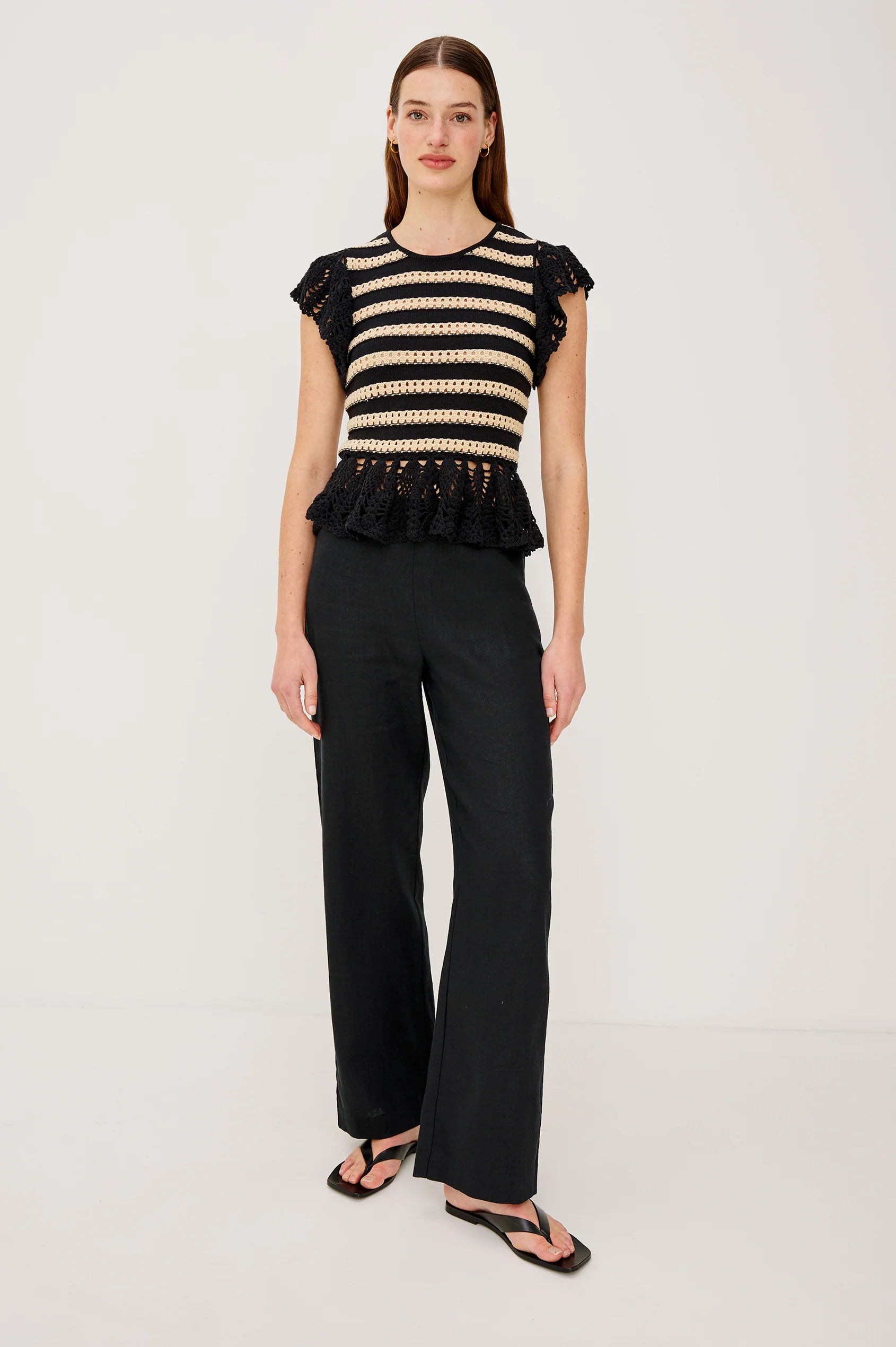 Woman wearing a black and beige striped top with ruffled details and black pants on a white background