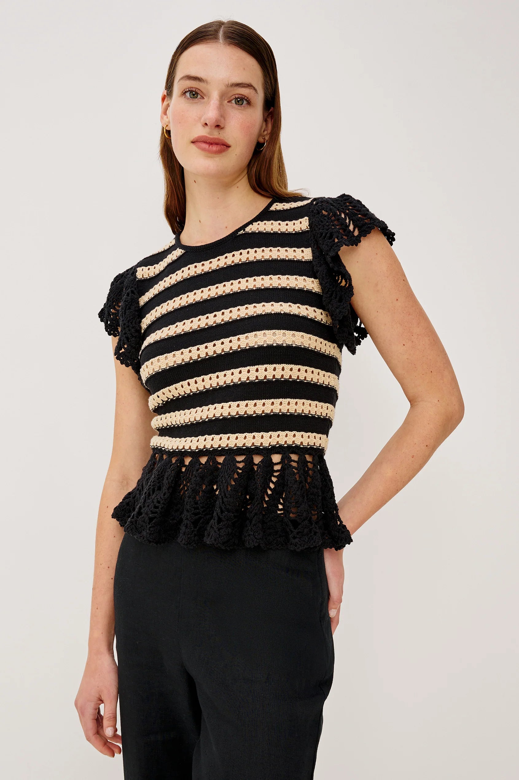 Woman wearing a black and beige striped top with ruffled details on a white background