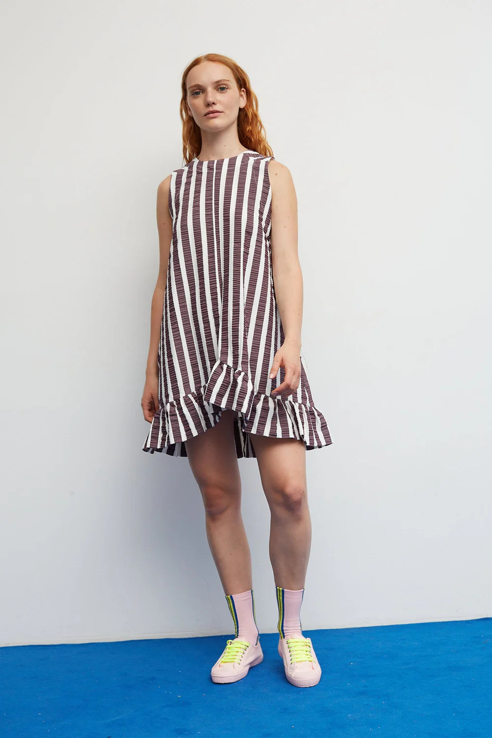 Woman wearing a striped dress standing on a blue floor with a white wall background