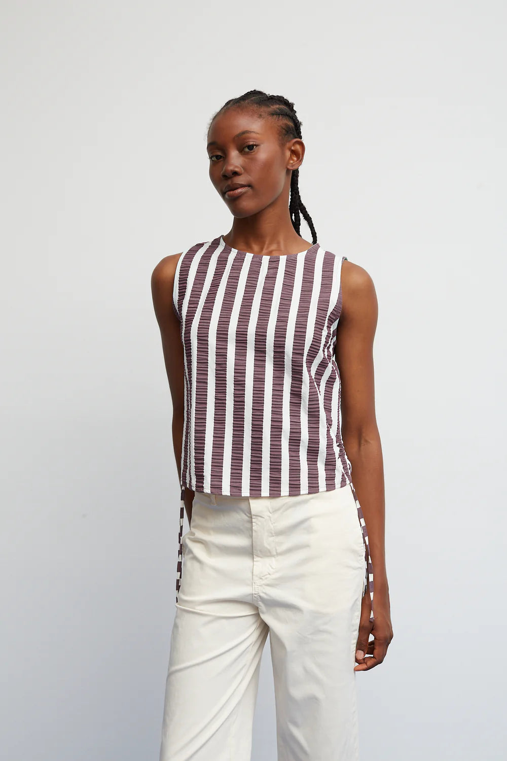 Woman wearing a striped sleeveless top and white pants against a plain background