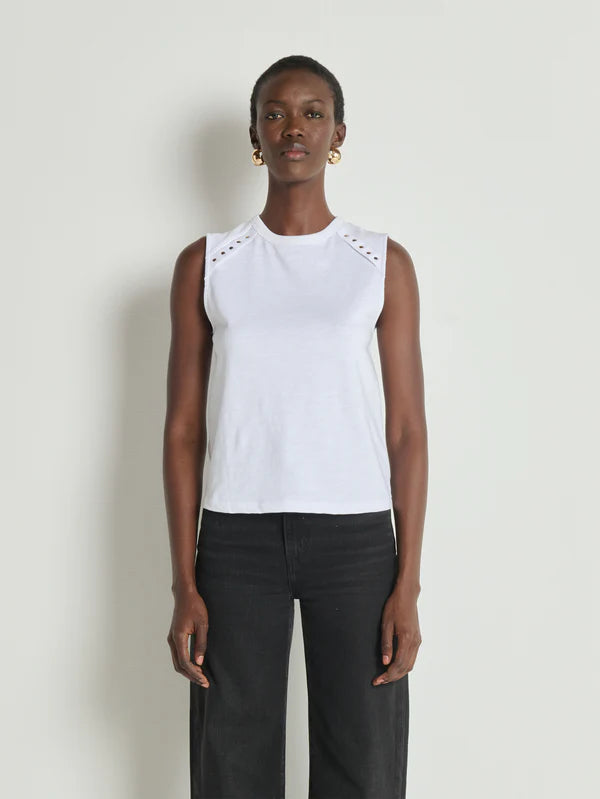 Woman wearing a white sleeveless top with decorative cutouts and black pants on a plain background