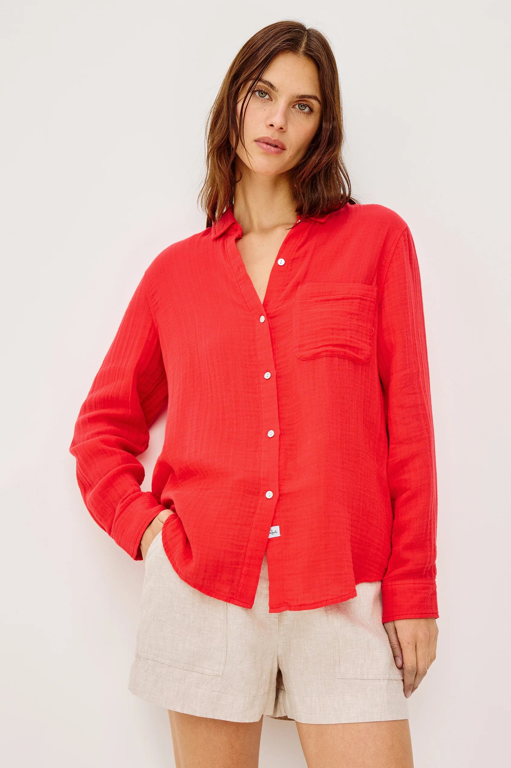 Woman wearing a red button-up shirt and beige shorts on a white background