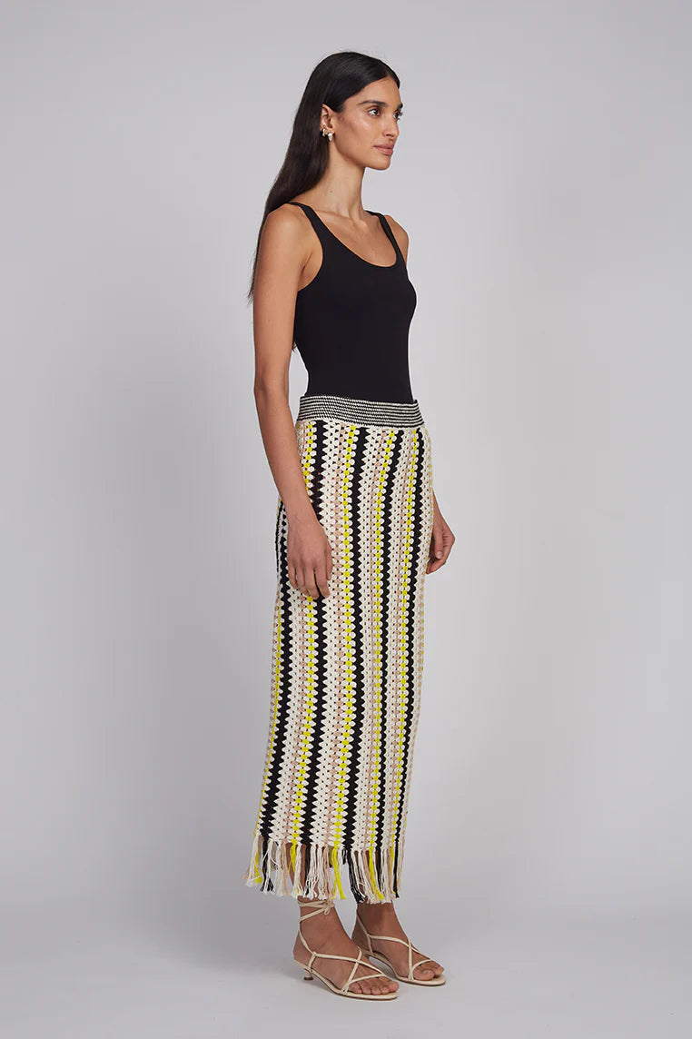 Woman wearing a black tank top and a long, patterned skirt on a gray background