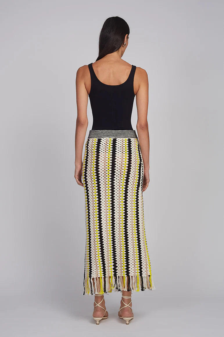 Woman wearing a black tank top and a long, patterned skirt on a gray background