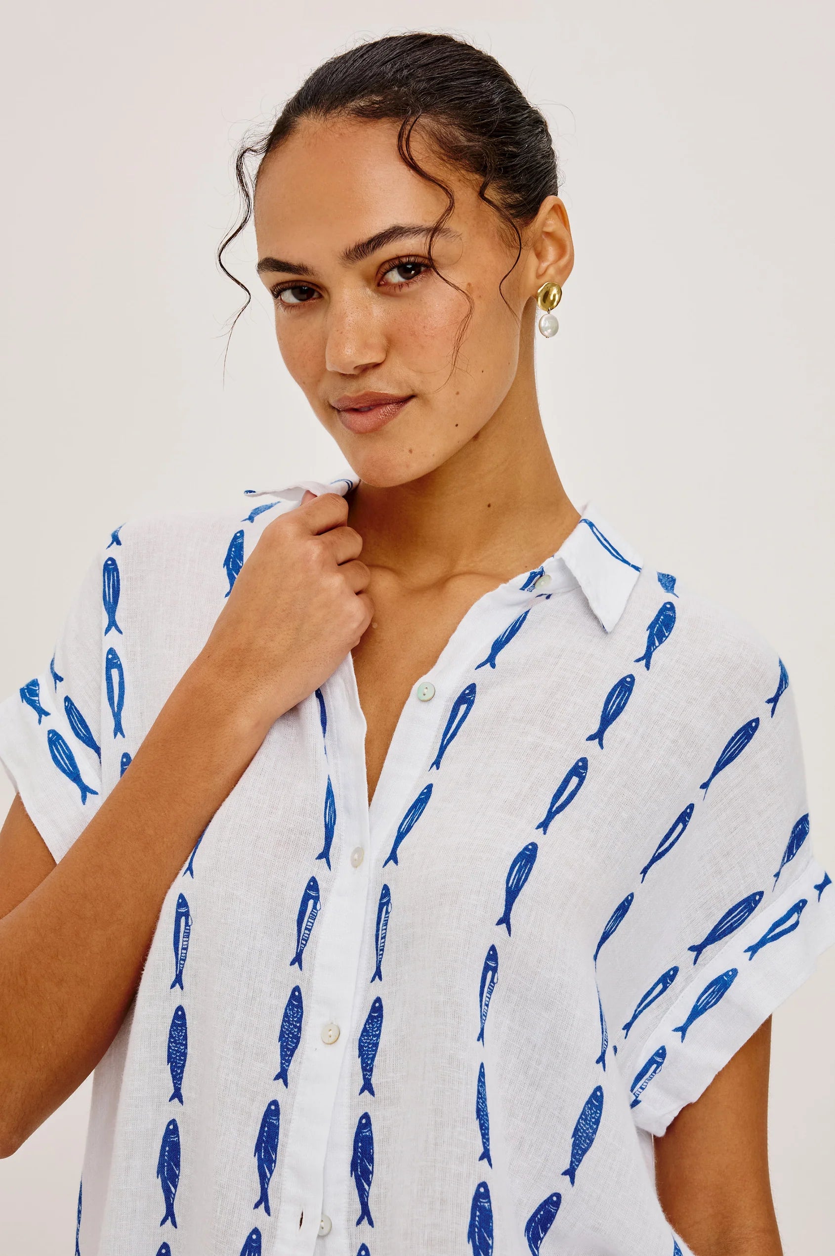 Woman wearing a white shirt with blue fish pattern against a plain background