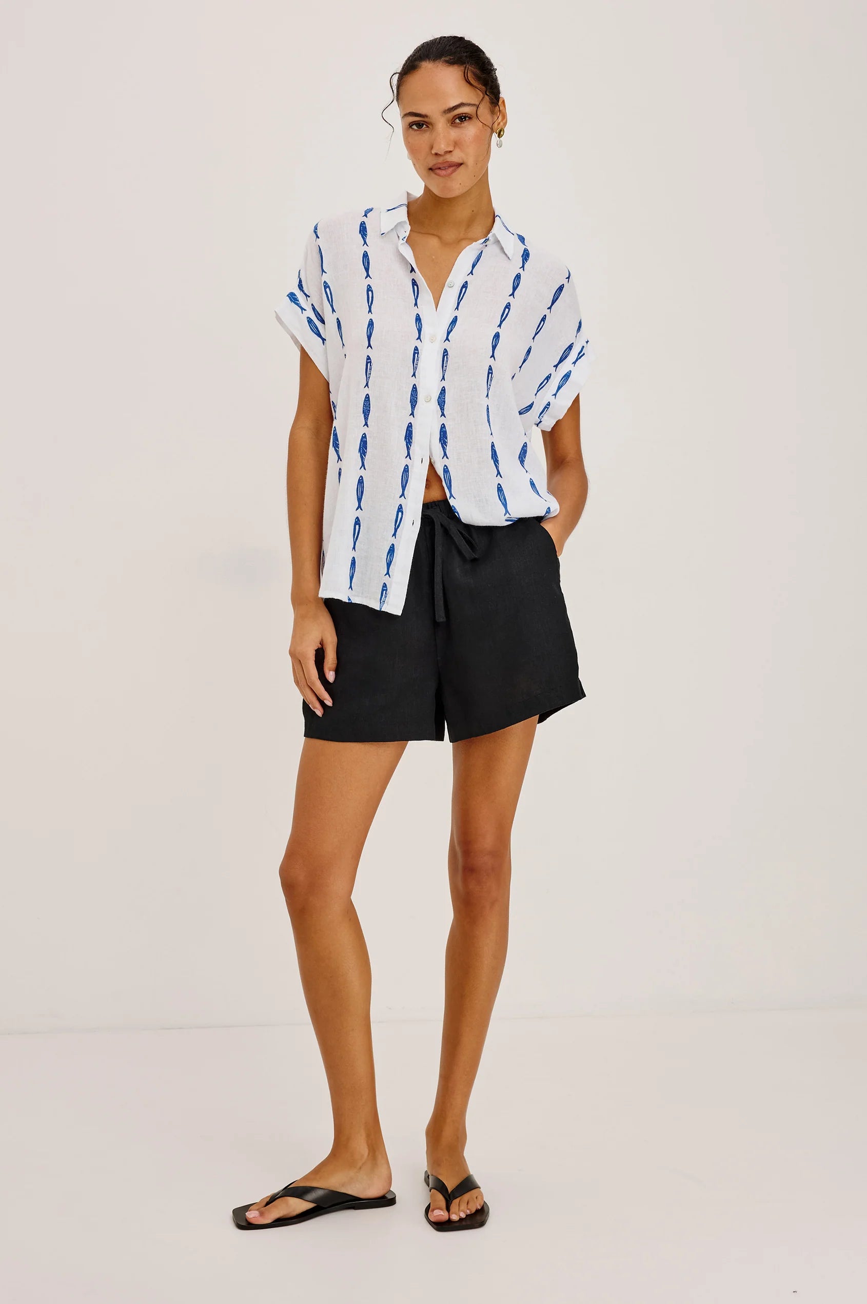 Woman wearing a white blouse with blue patterns and black shorts on a white background