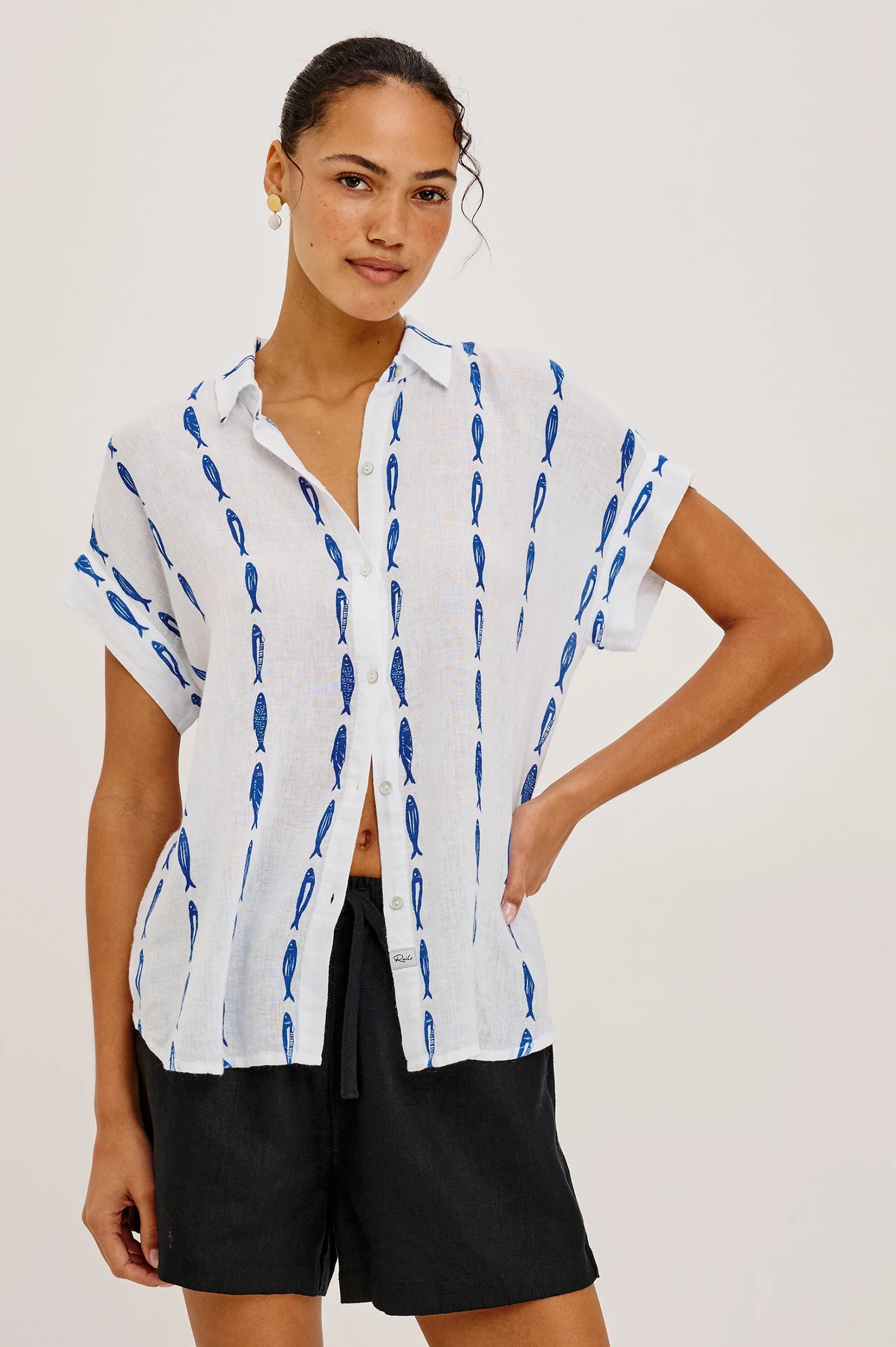 Woman wearing a white shirt with blue patterns and black shorts on a plain background