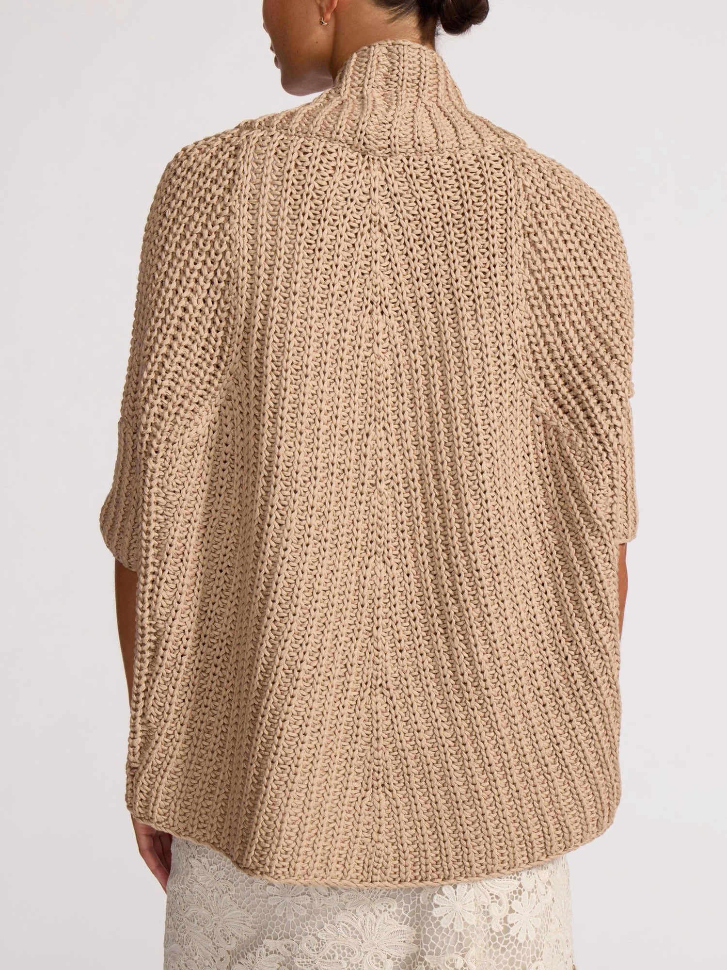 Beige knitted poncho worn by a person on a white background