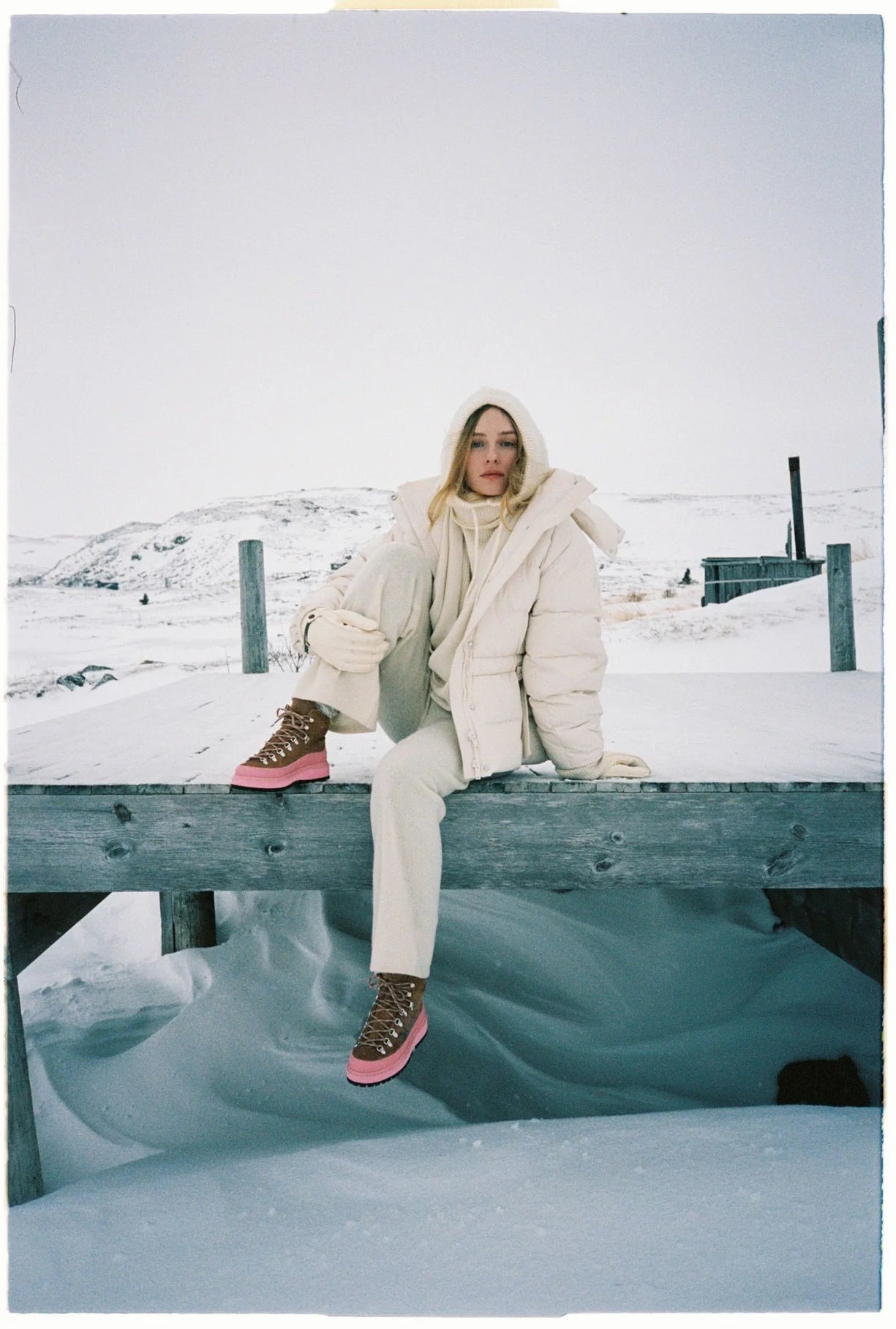 Person sitting on a snowy dock wearing a large white puffer coat.