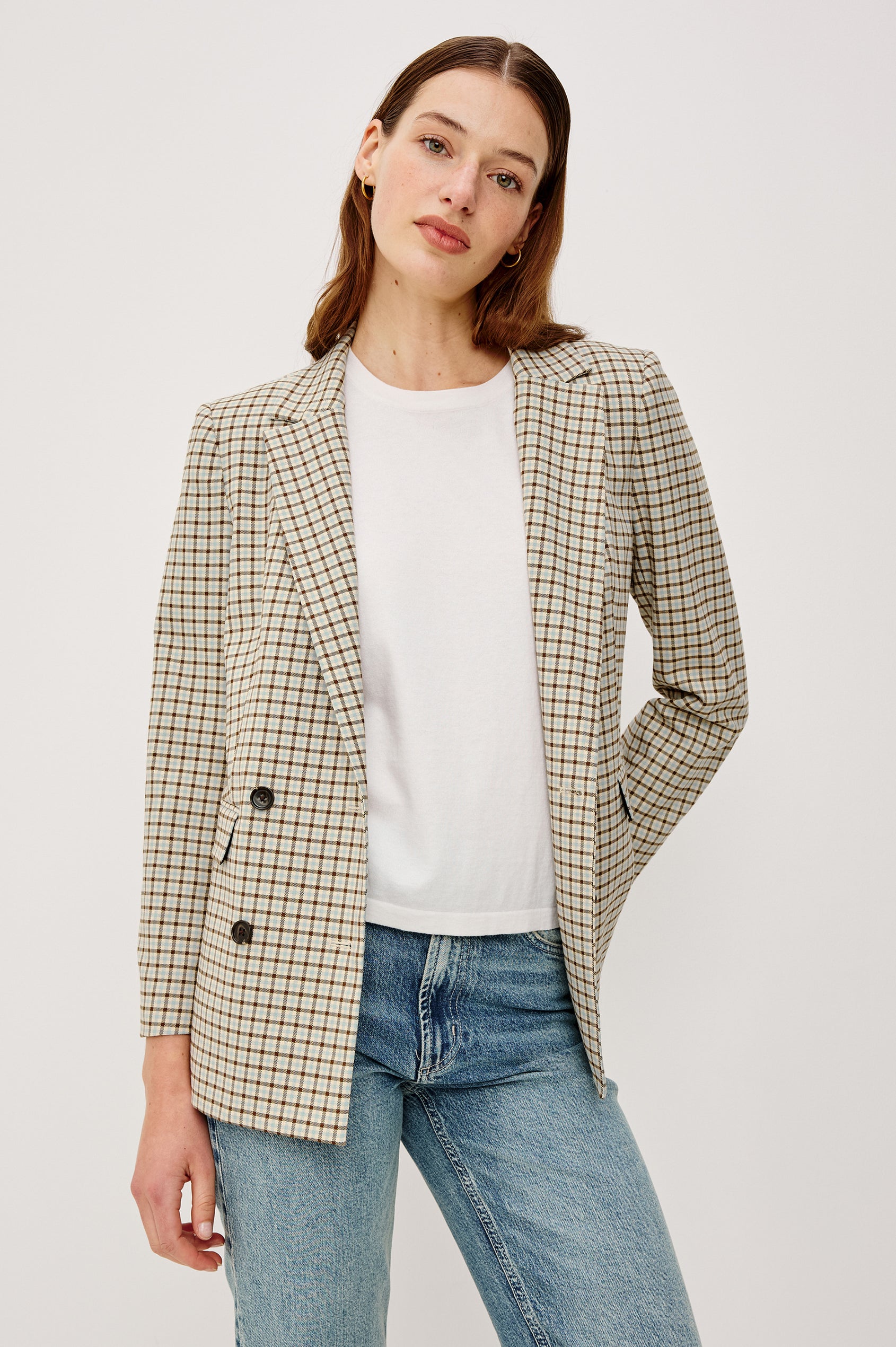 Woman wearing a checkered blazer over a white shirt and blue jeans on a plain background