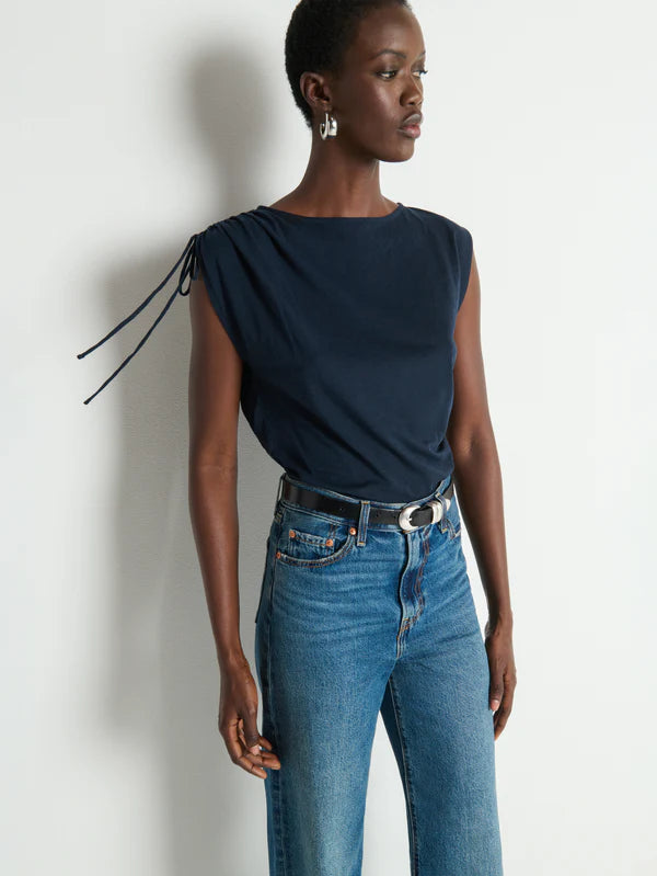 Woman wearing a navy top and blue jeans against a white background