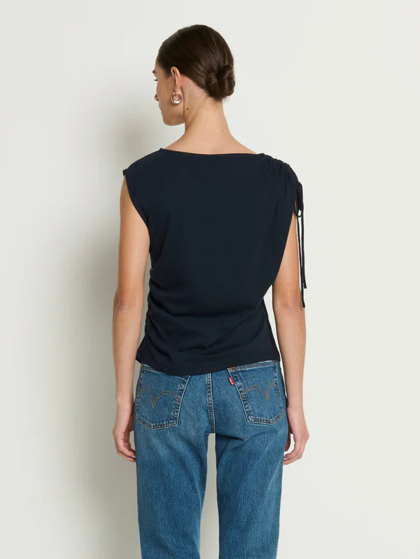 Person wearing a navy blue sleeveless top and blue jeans on a plain background
