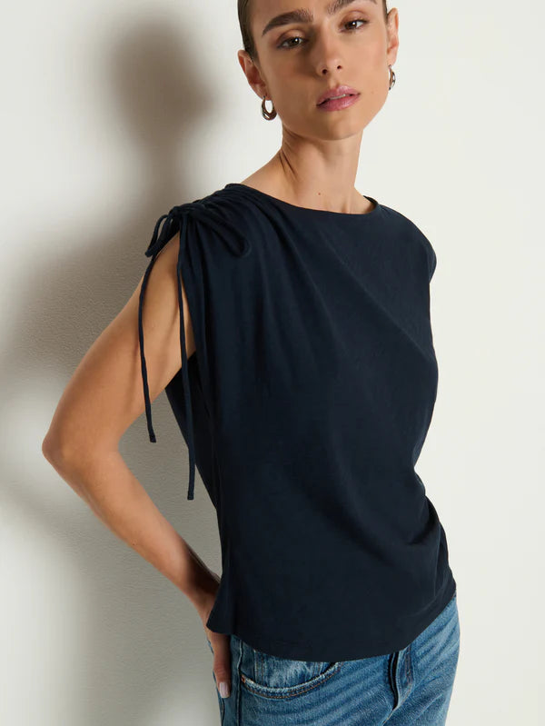 Woman wearing a black sleeveless top with tie details against a neutral background