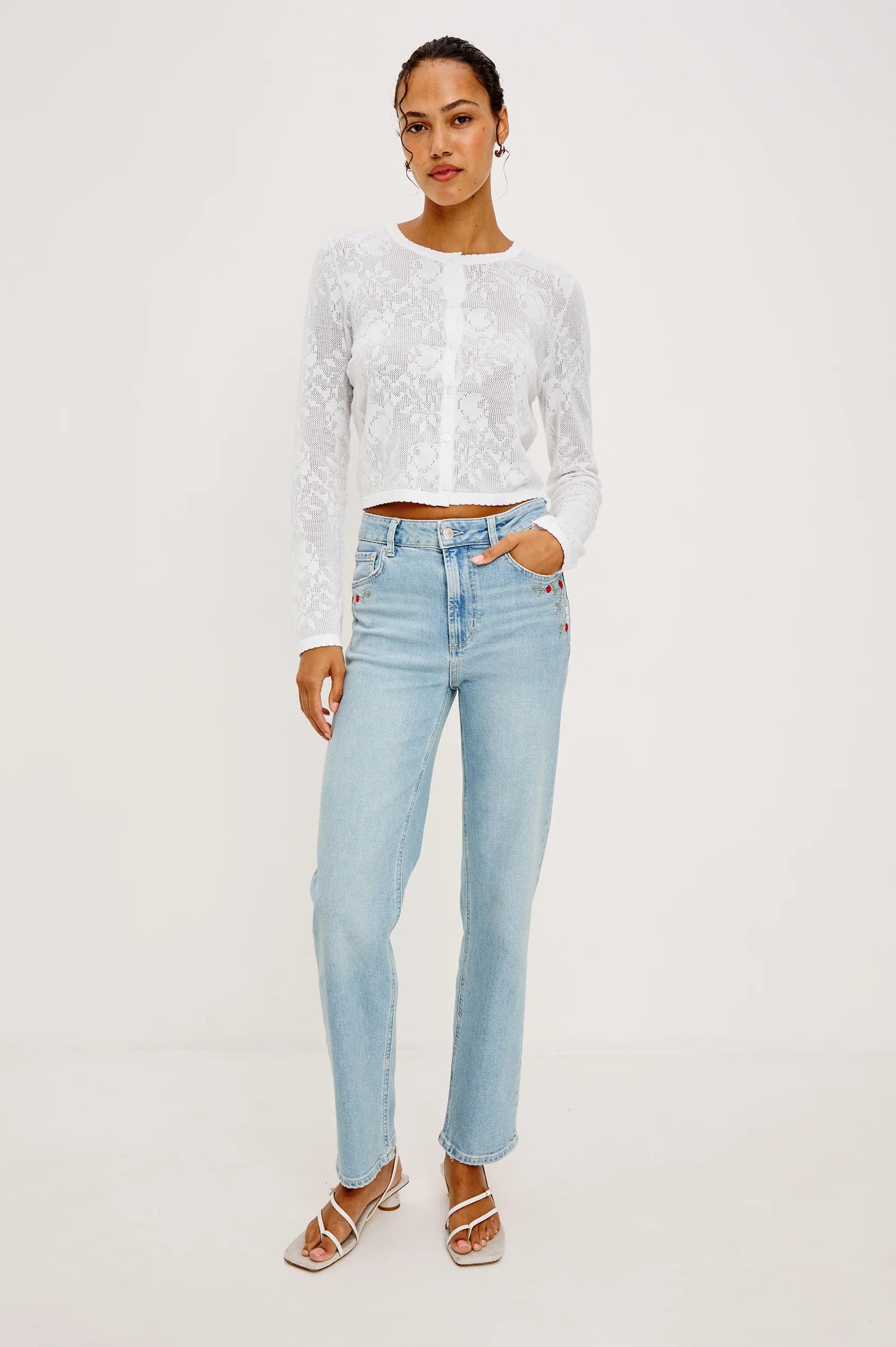 Woman wearing a white lace top and light blue jeans on a white background