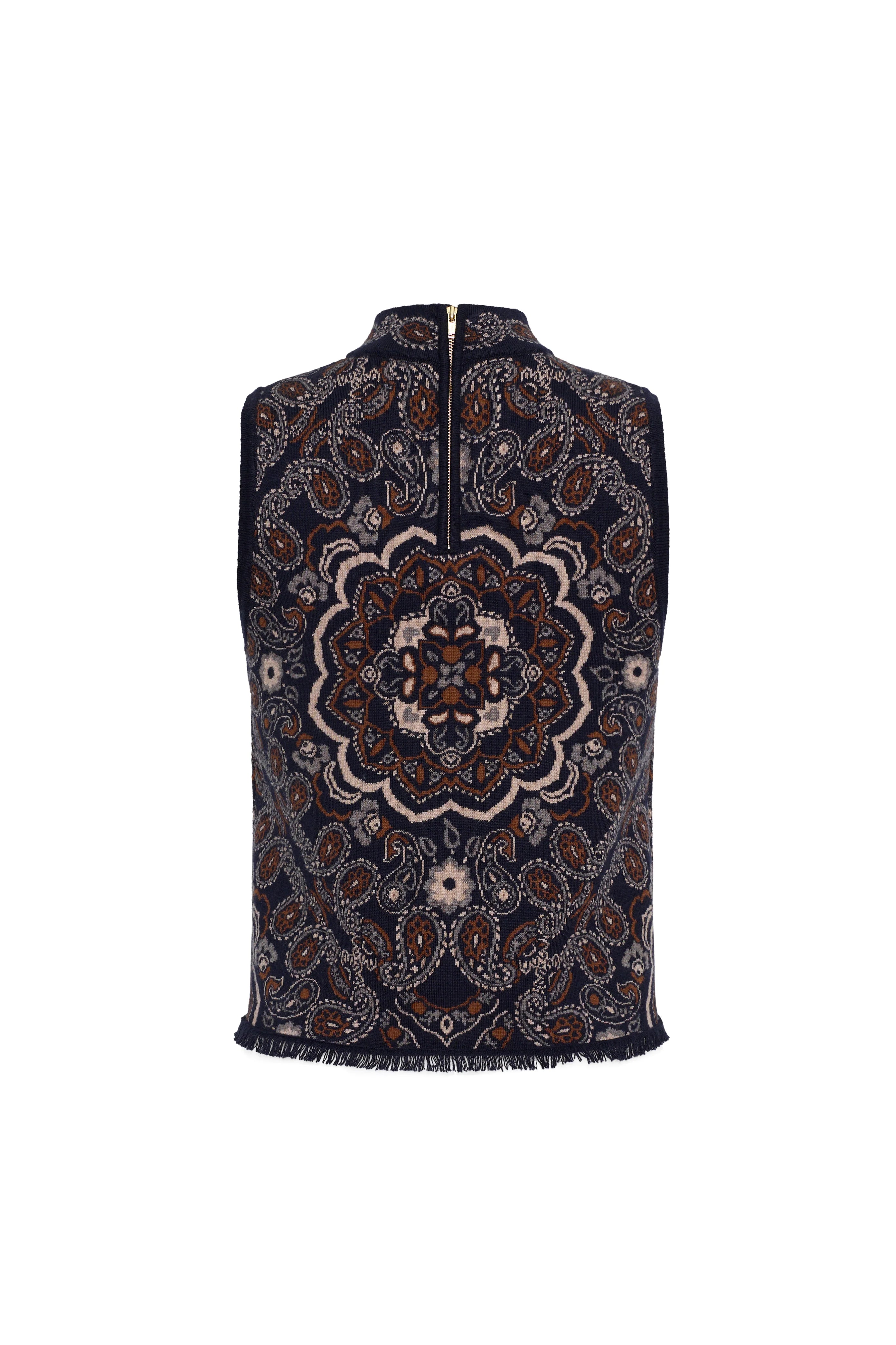 A sleeveless zip-front vest with a high mock neck, featuring an intricate navy blue, brown, and beige mandala pattern and fringed edges, shown against a plain white background.
