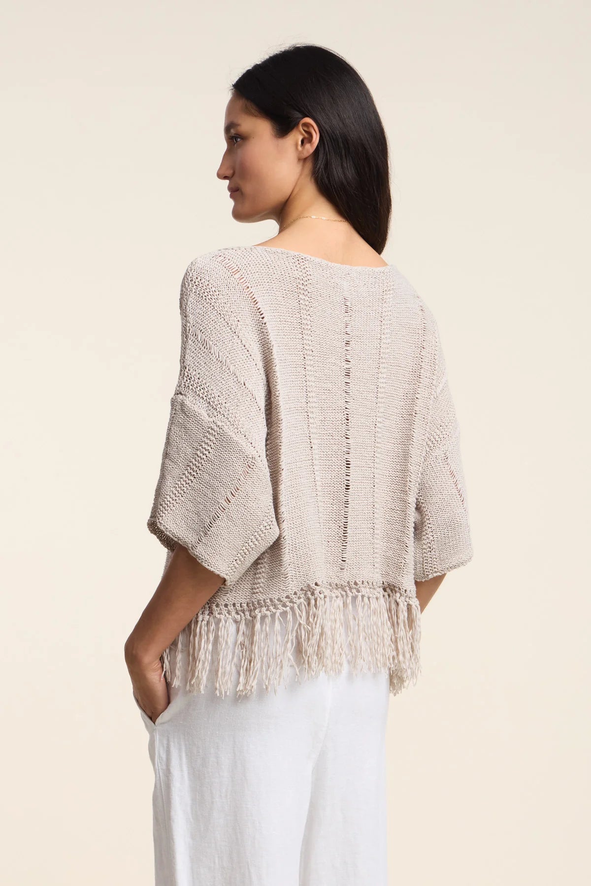 Woman wearing a beige knitted top with a plain background