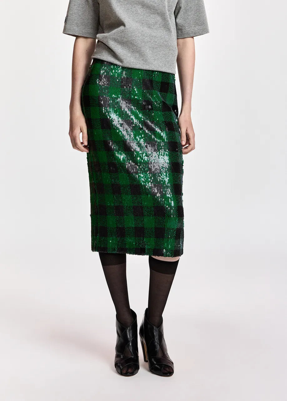 A model wearing a green and black sequined plaid midi skirt, styled with a gray t-shirt, black tights, and black ankle boots against a plain light background.