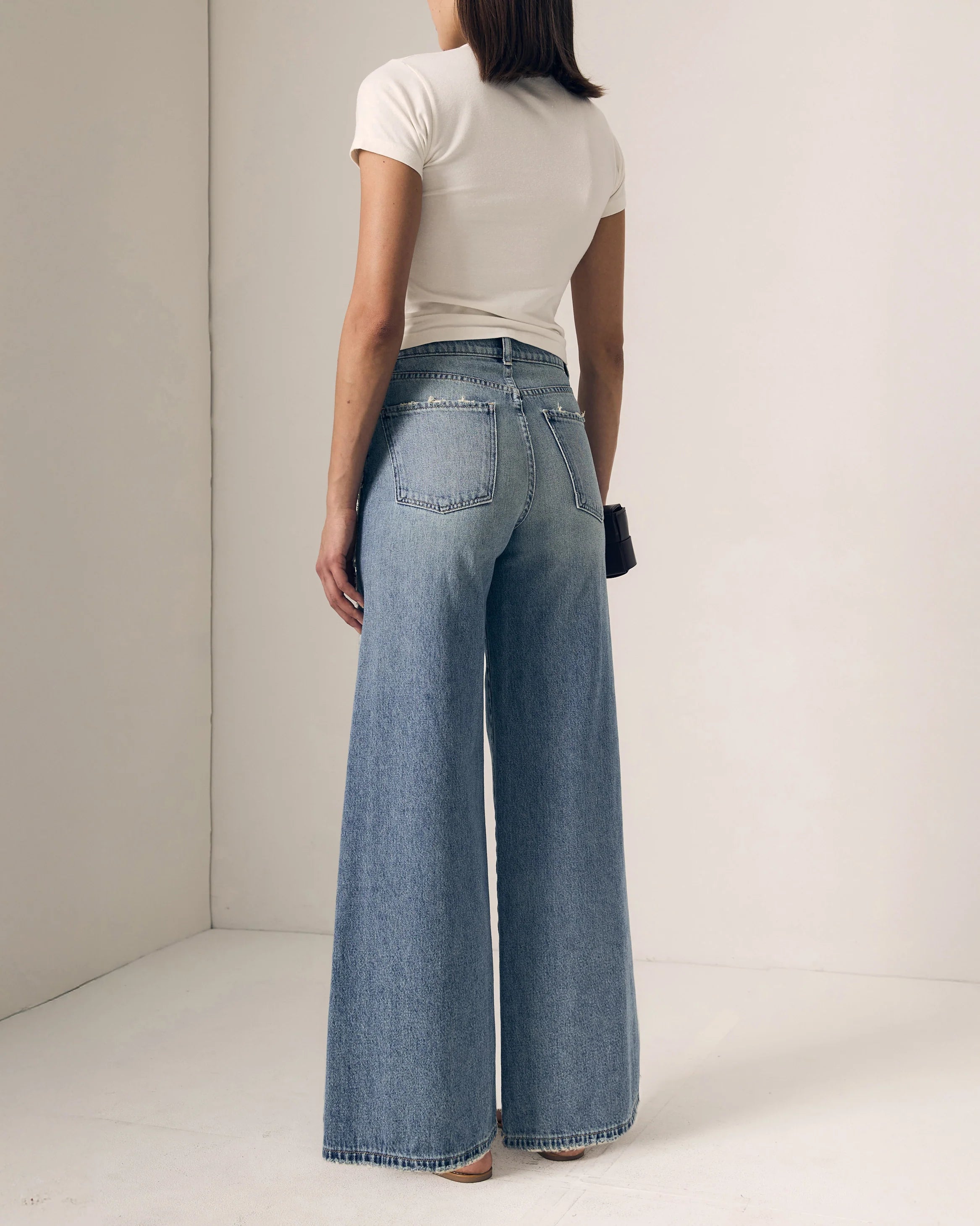 Person wearing blue wide-leg jeans and a white top against a plain background