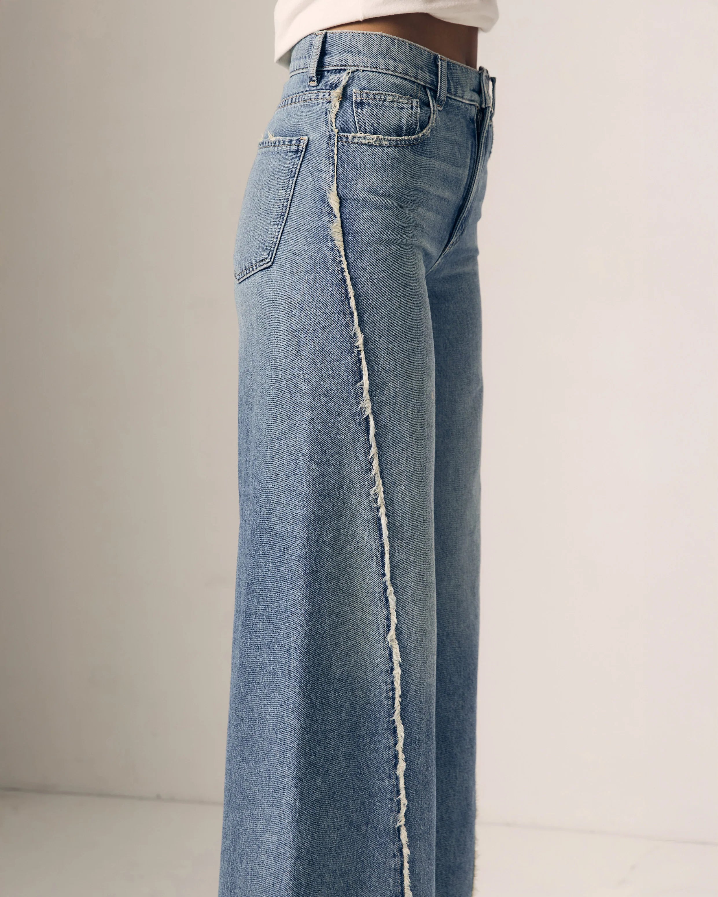 Blue jeans with a frayed hem on a plain background