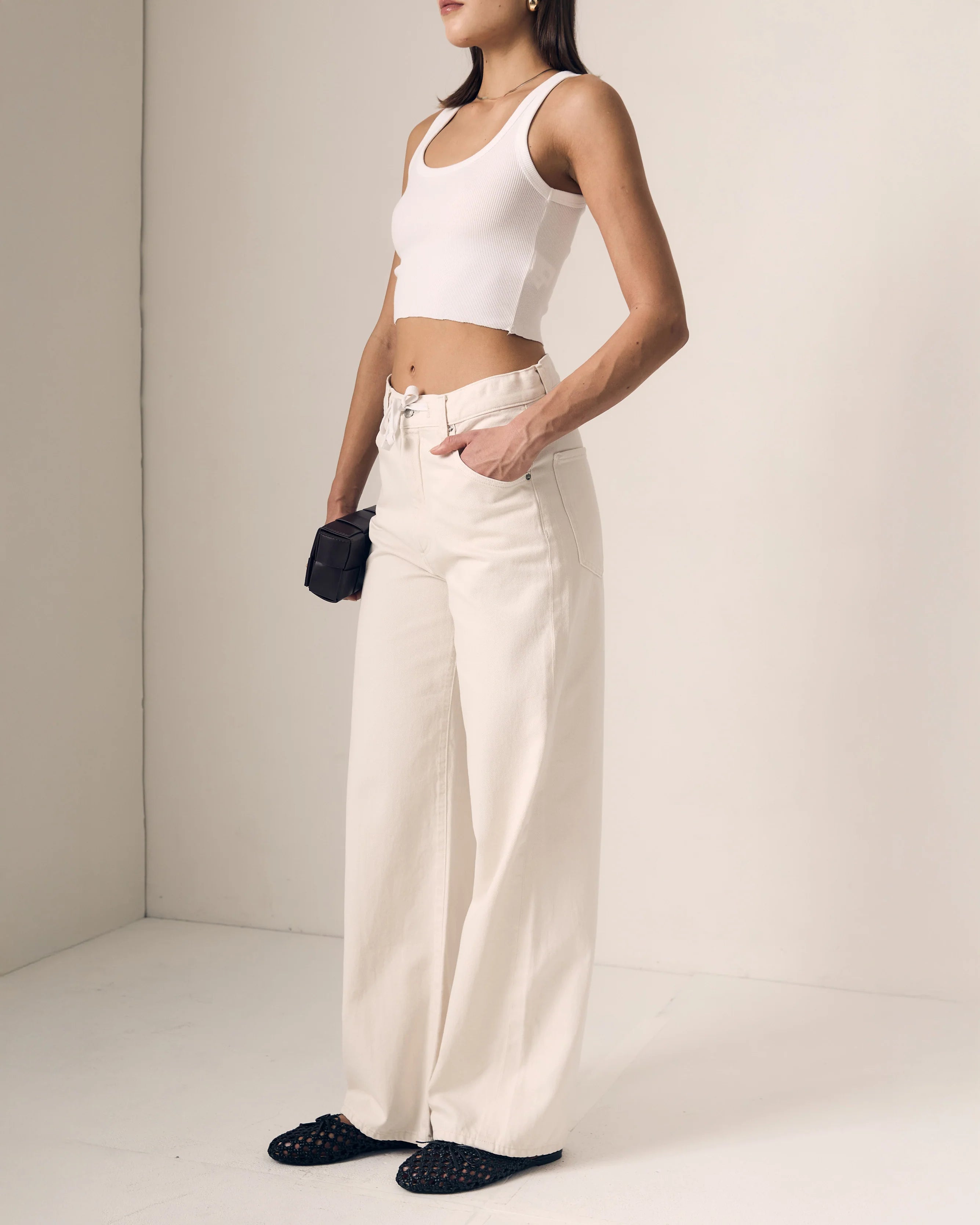 Person wearing a white sleeveless top and cream-colored pants against a plain background