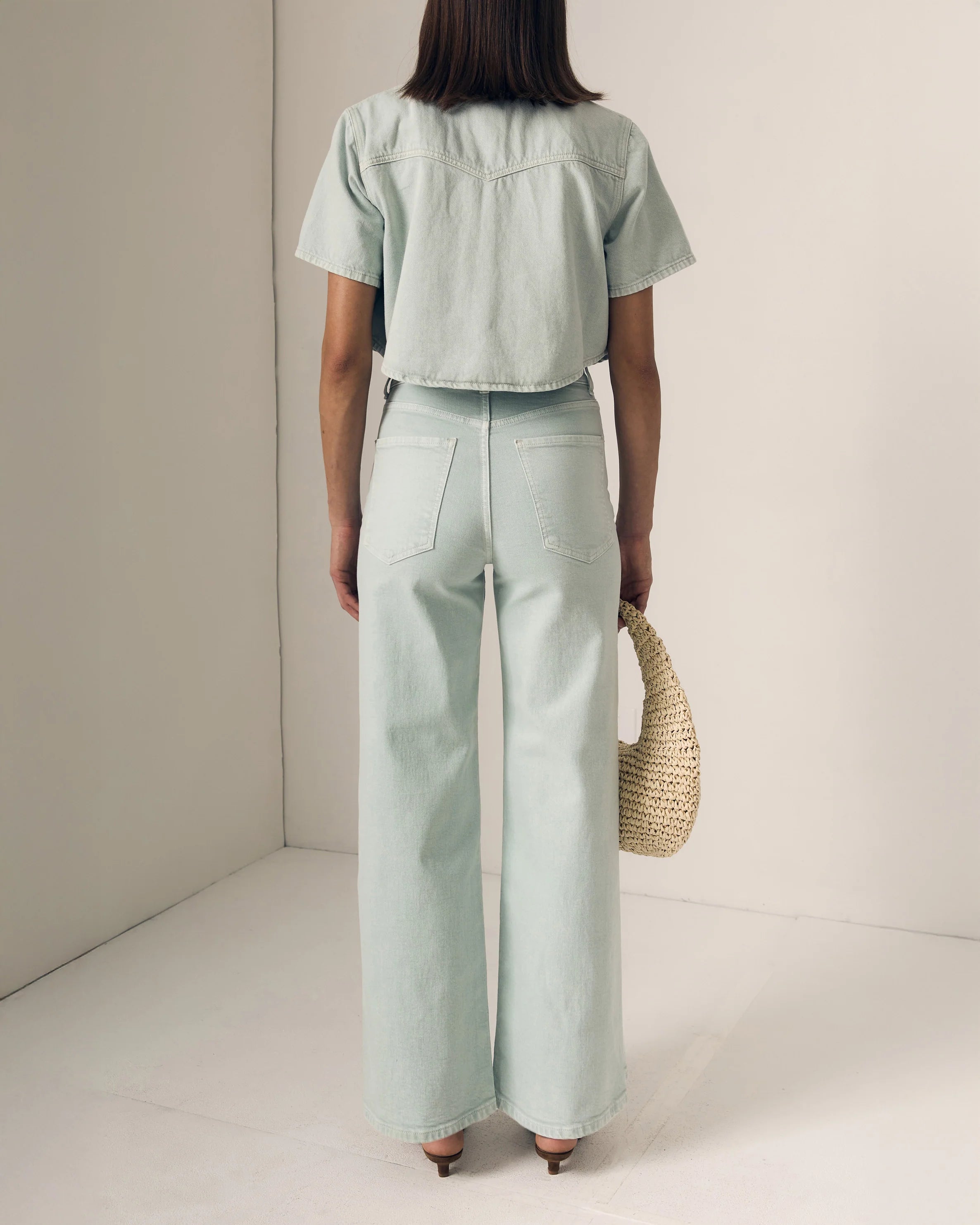 Person wearing a light green outfit with wide-leg pants and a matching top, holding a woven bag.