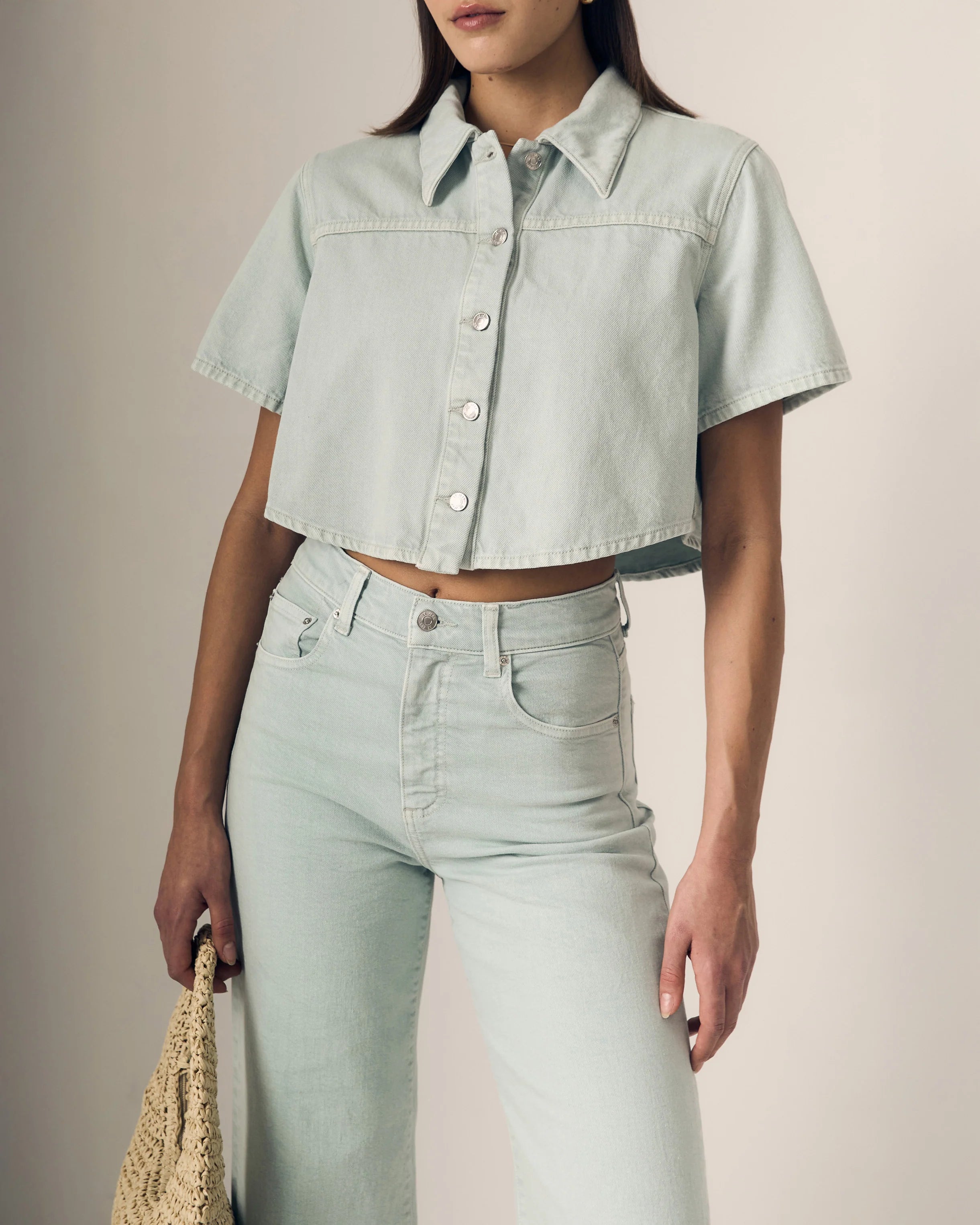 Person wearing a light blue denim shirt and jeans against a neutral background