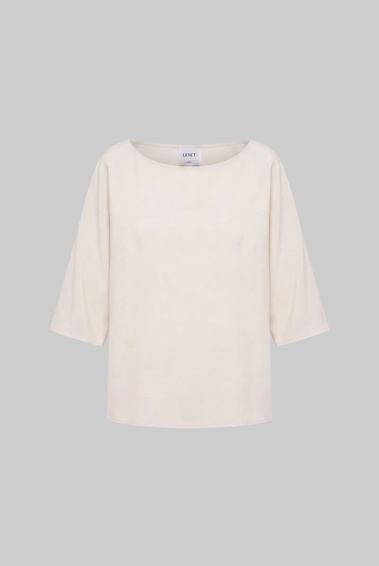 An off-white three-quarter sleeve top with a wide boat neckline, displayed against a solid gray background.