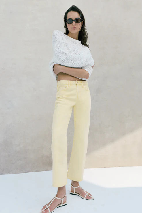 Woman wearing a white sweater and yellow pants against a neutral background