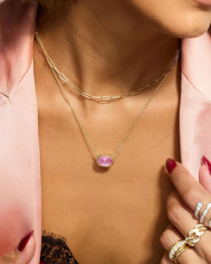 Gold necklace with a pink gemstone worn by a person in a pink jacket.