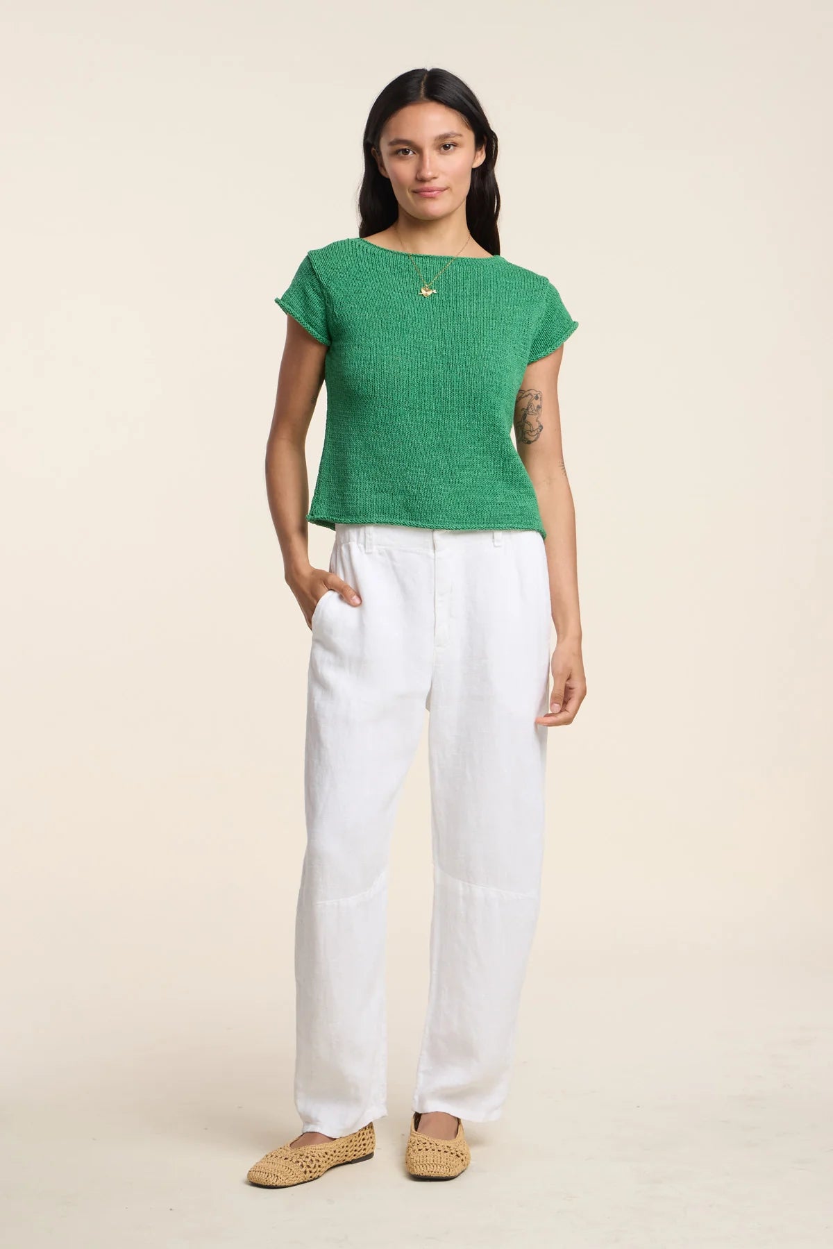 Woman wearing a green top and white pants on a beige background