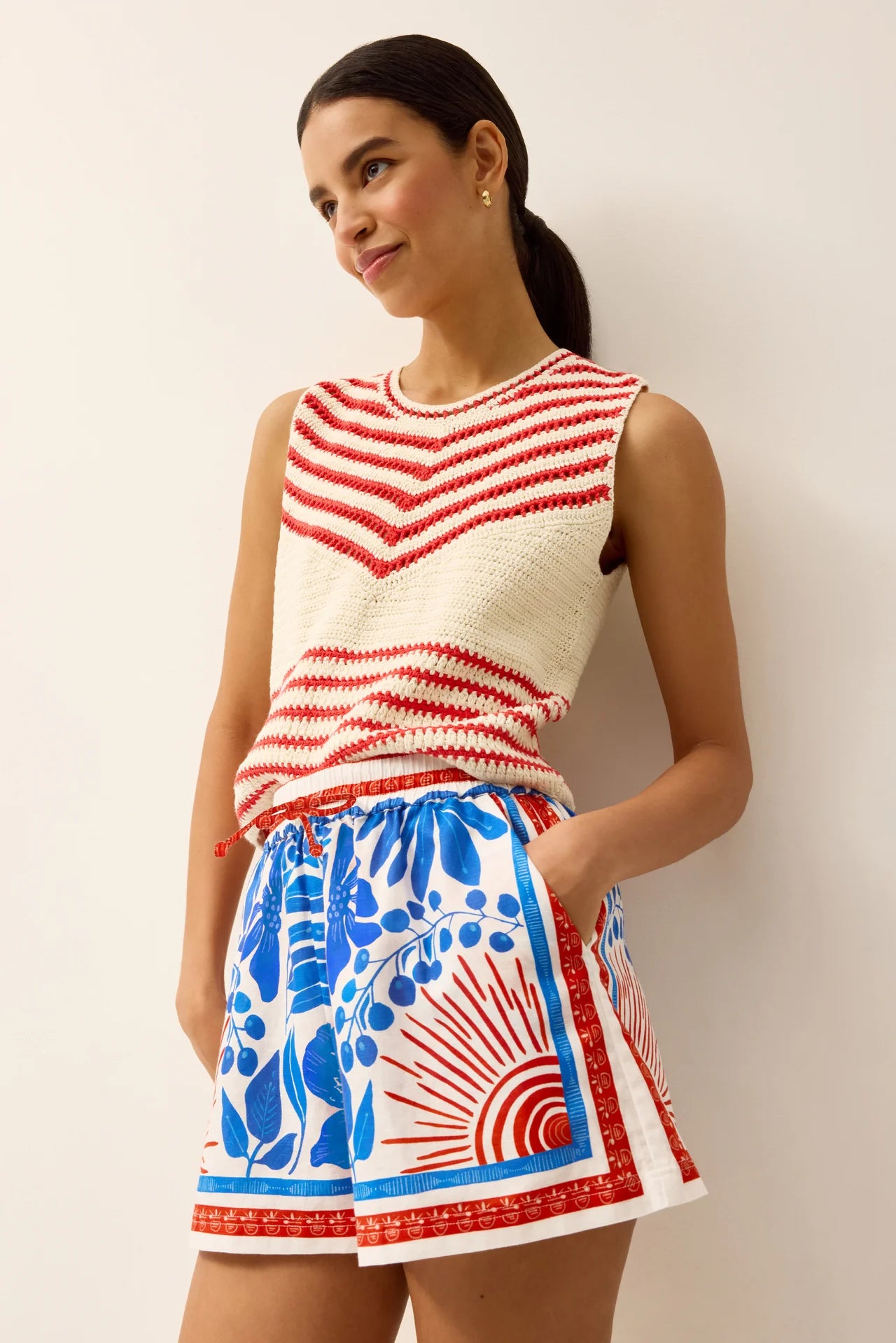 Woman wearing a red and white striped sleeveless top and a blue and white patterned skirt against a plain background.
