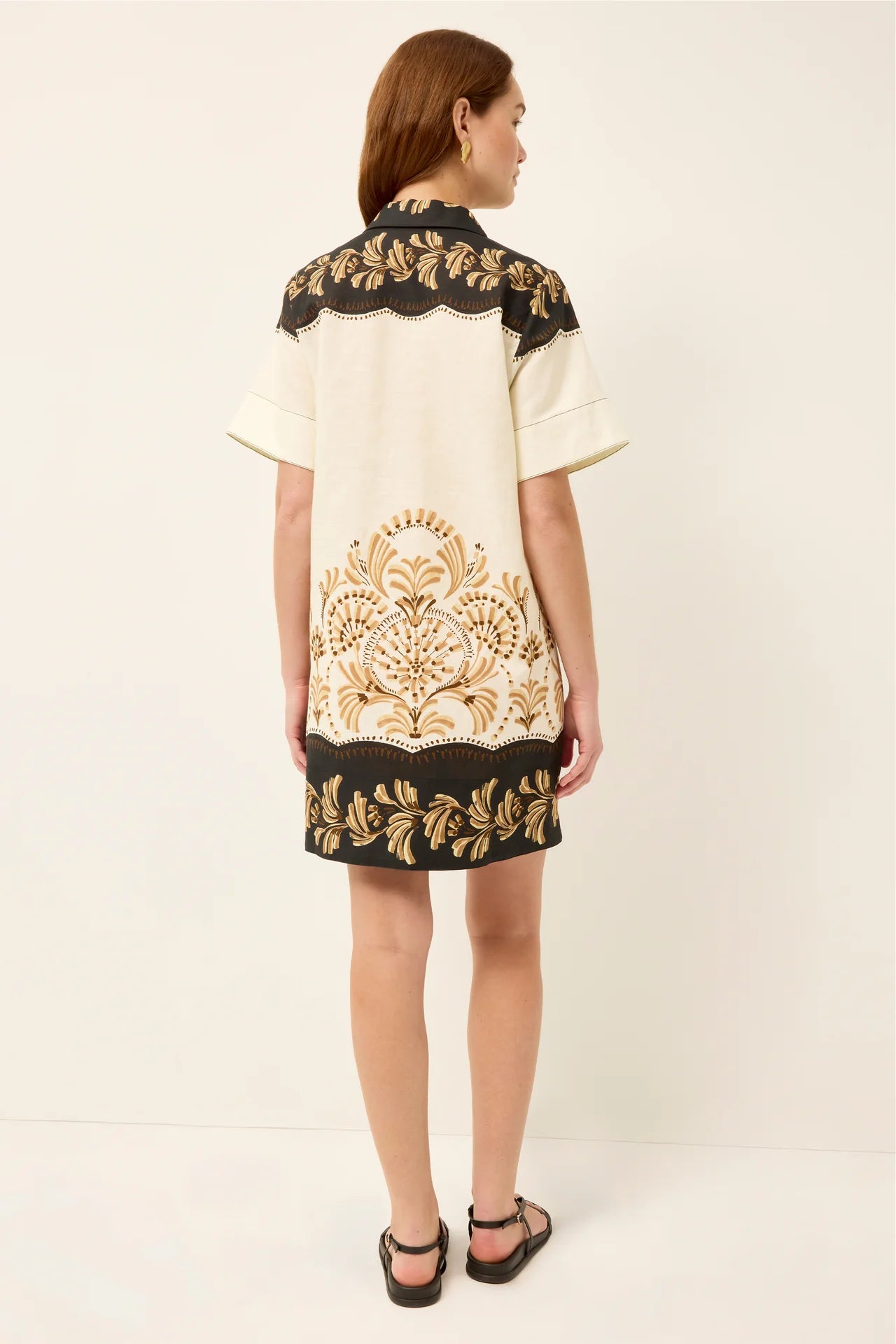 Woman wearing a cream dress with black and gold embroidery on a white background