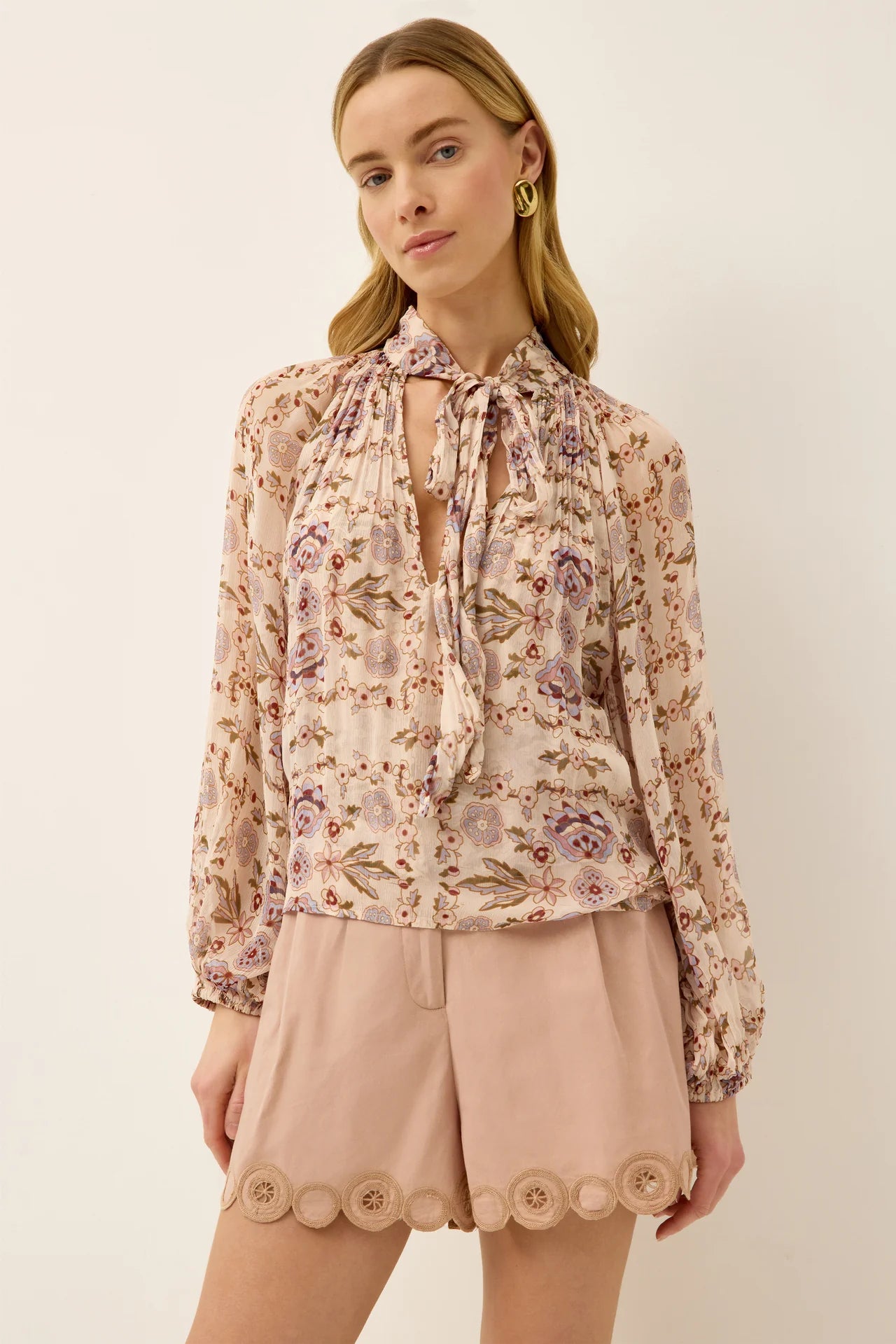 Woman wearing a floral blouse and beige shorts on a plain background