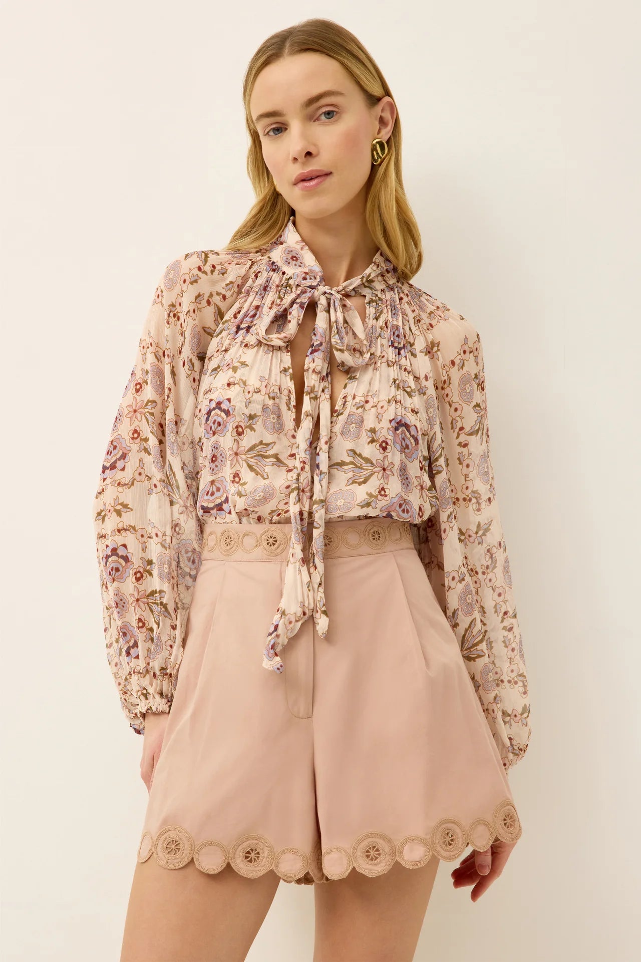 Woman wearing a floral blouse and pink shorts against a white background