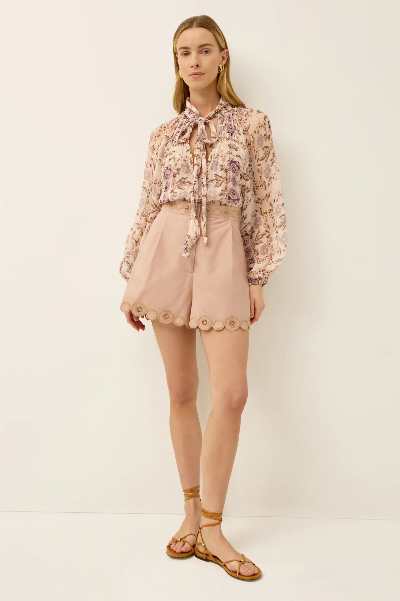 Woman wearing a floral blouse and beige shorts against a white background