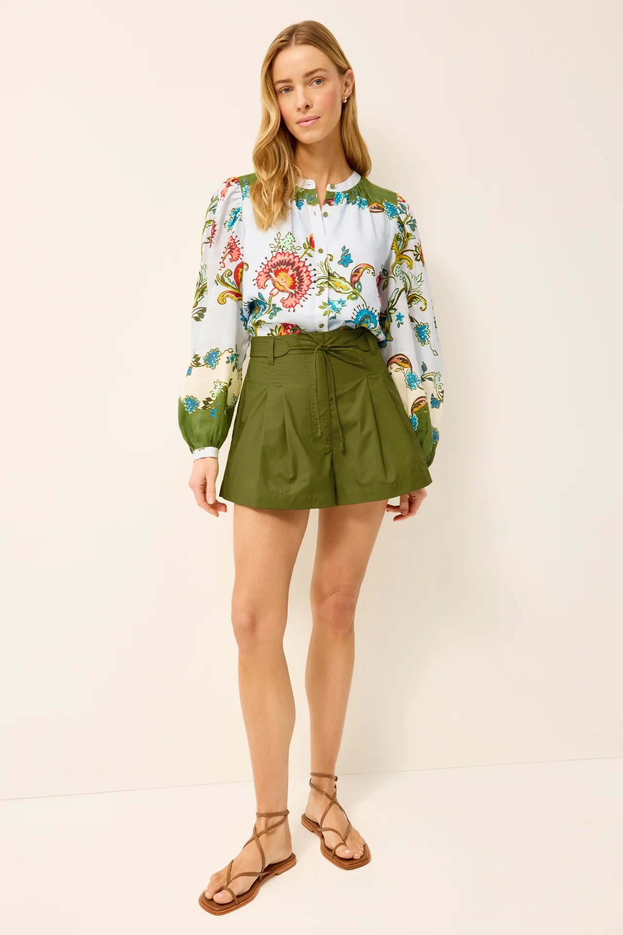 Woman wearing a floral blouse and green shorts against a white background